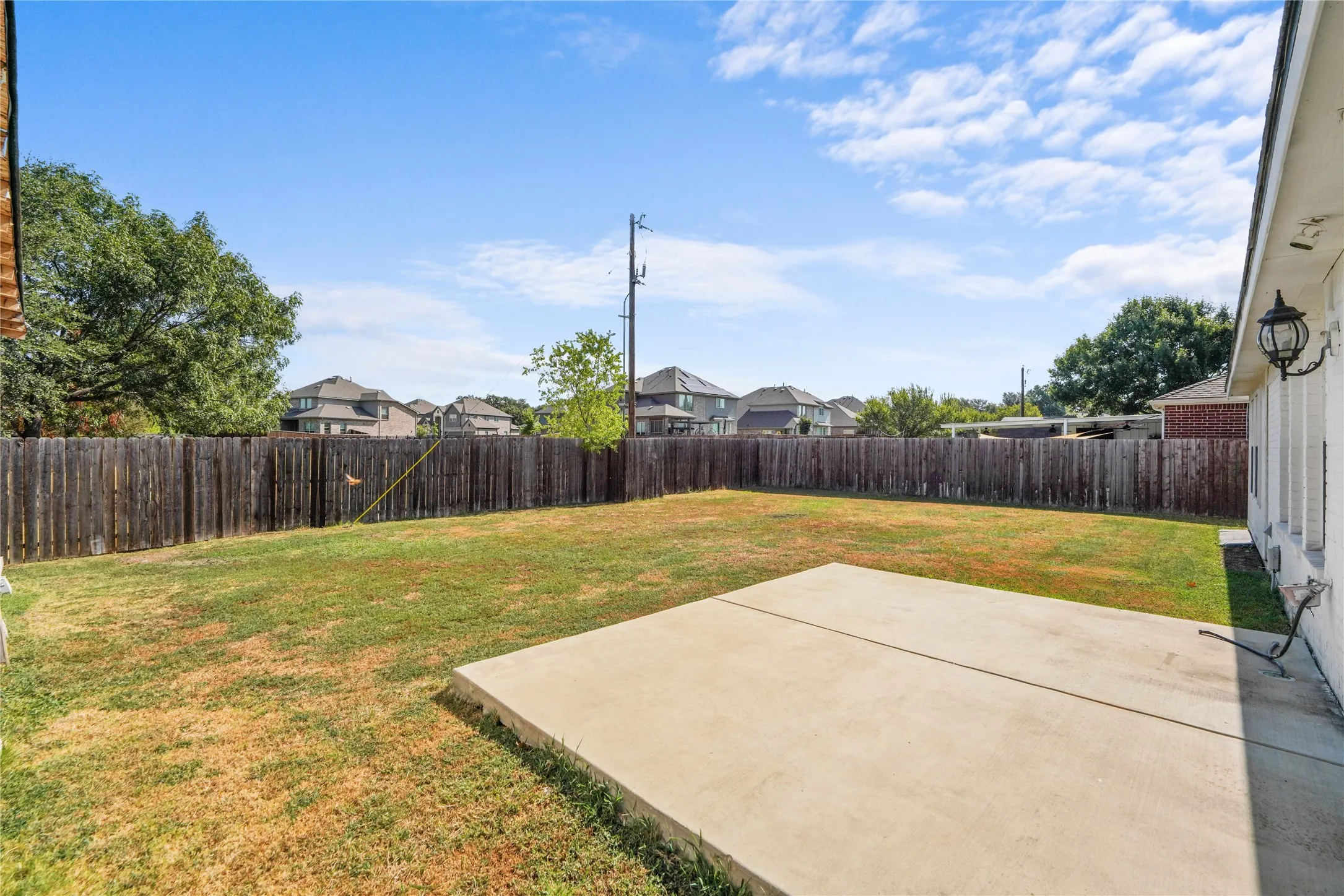 Expansive backyard with a wood privacy fence, concrete patio, and exterior wall-mounted lighting