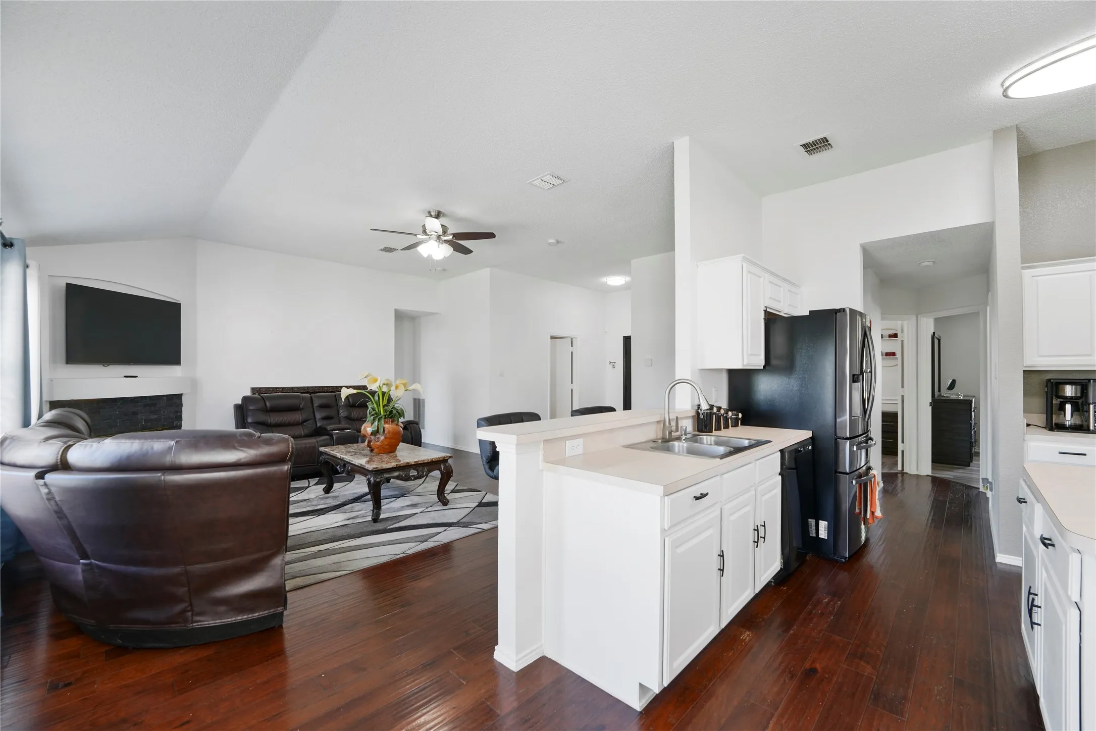 Vaulted ceiling, wood-finish flooring, white cabinetry, light-toned countertops, and a built-in kitchen sink