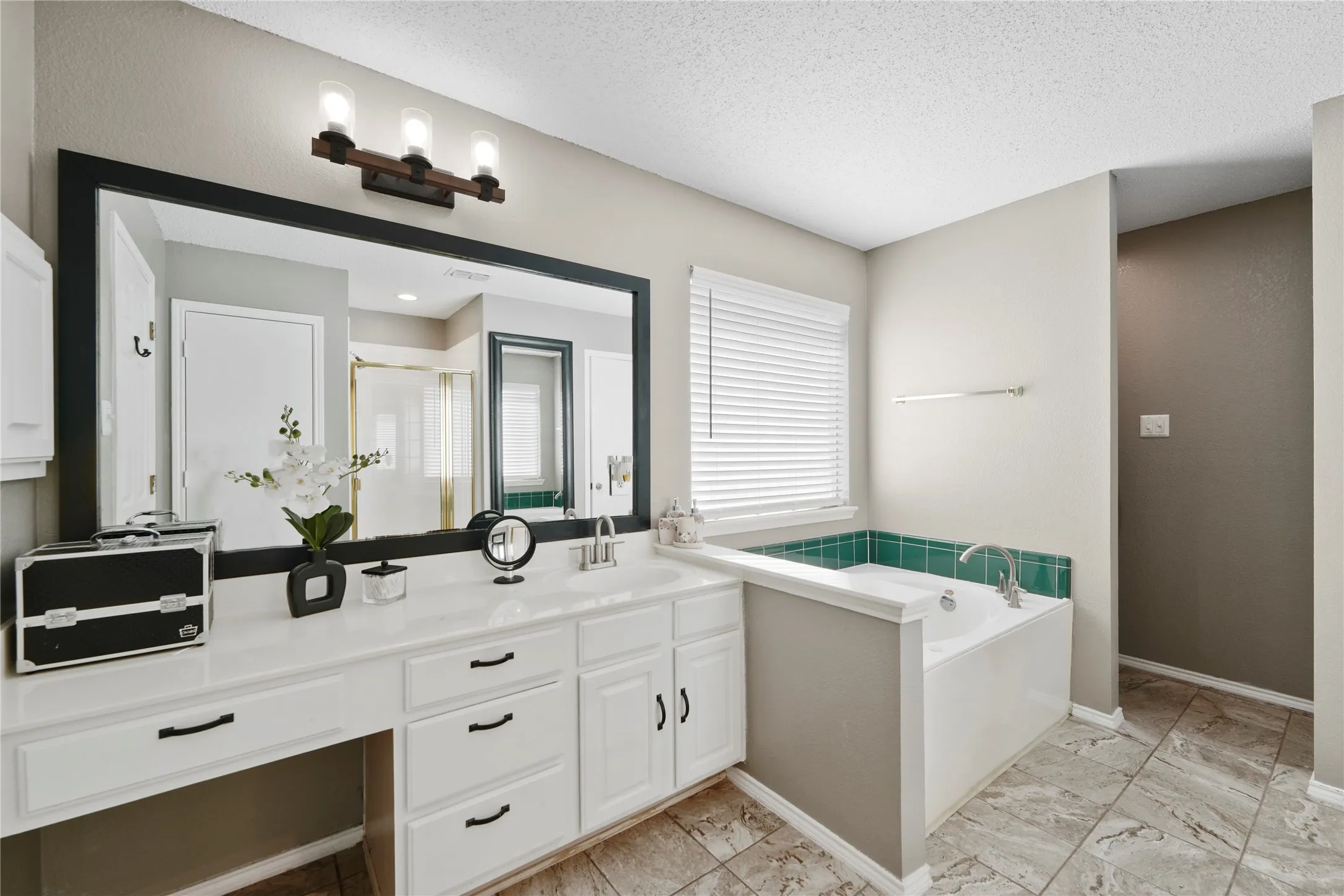Dual vanity with white cabinetry and dark hardware, integrated countertop with single sink, and a large framed mirror