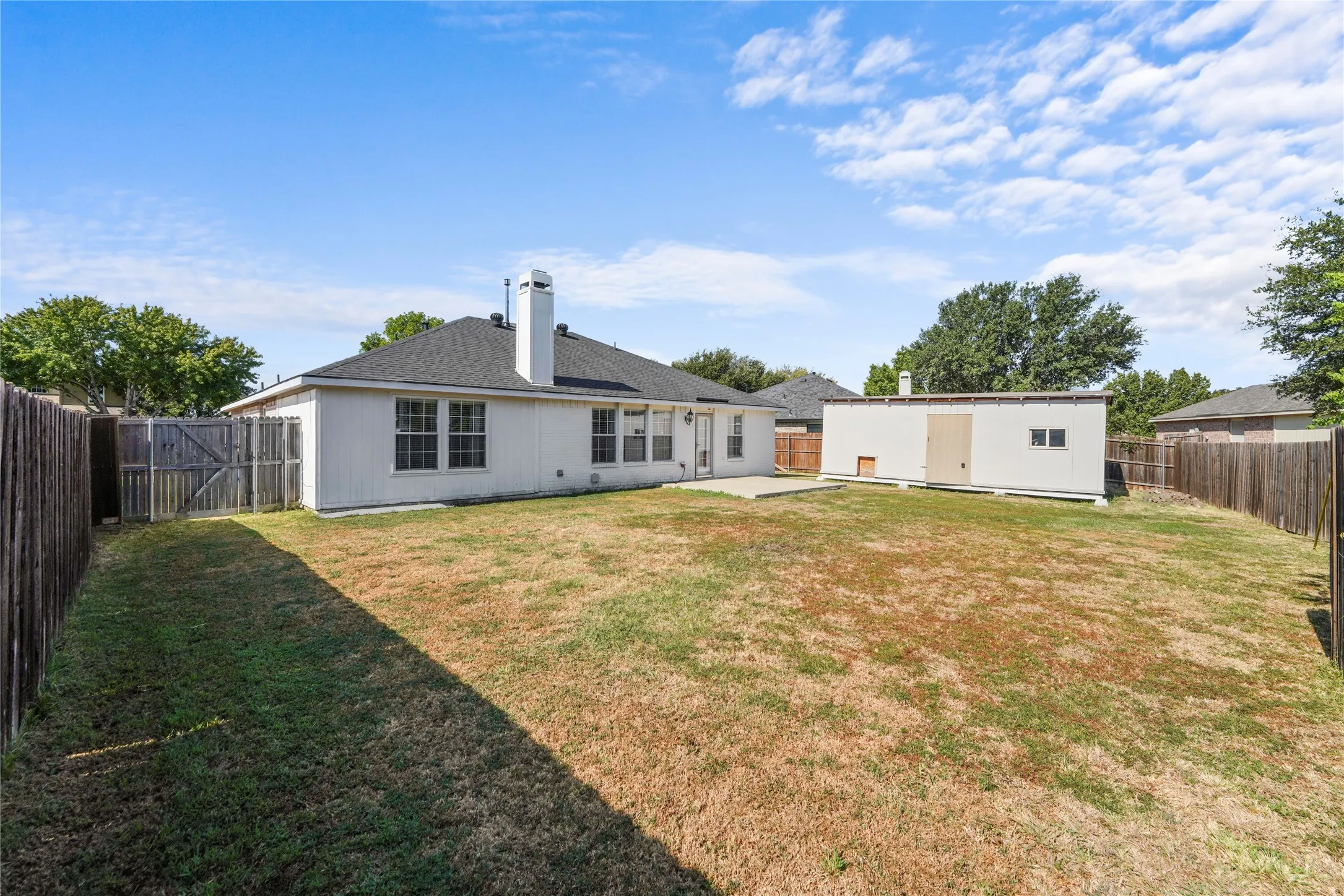 Expansive backyard featuring a privacy fence, concrete patio, and a standalone storage structure