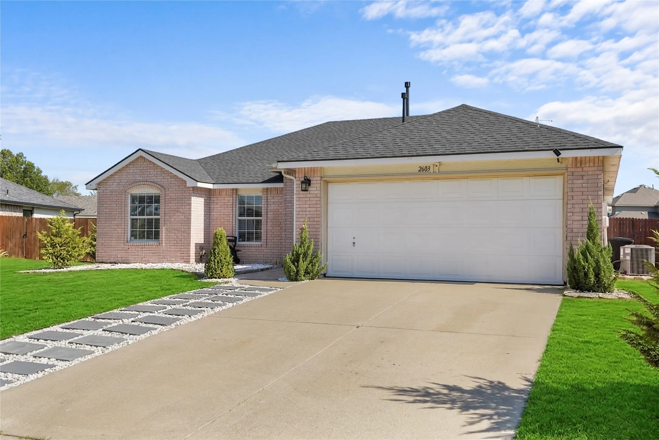 Brick facade, attached two-car garage, concrete driveway, stone paver pathway, and manicured lawn