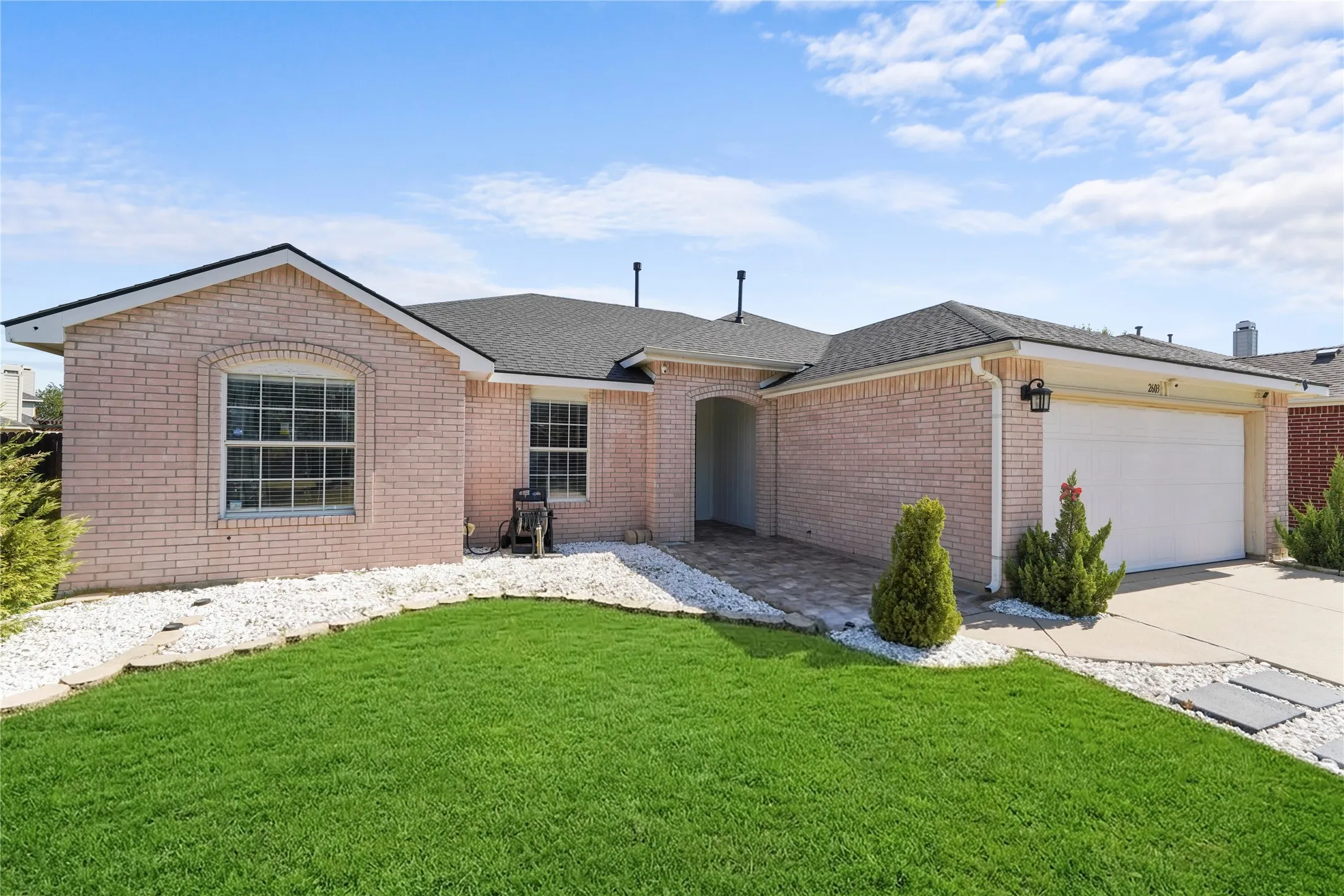 Pink brick exterior with a dark shingle roof, arched entryway, and an attached garage