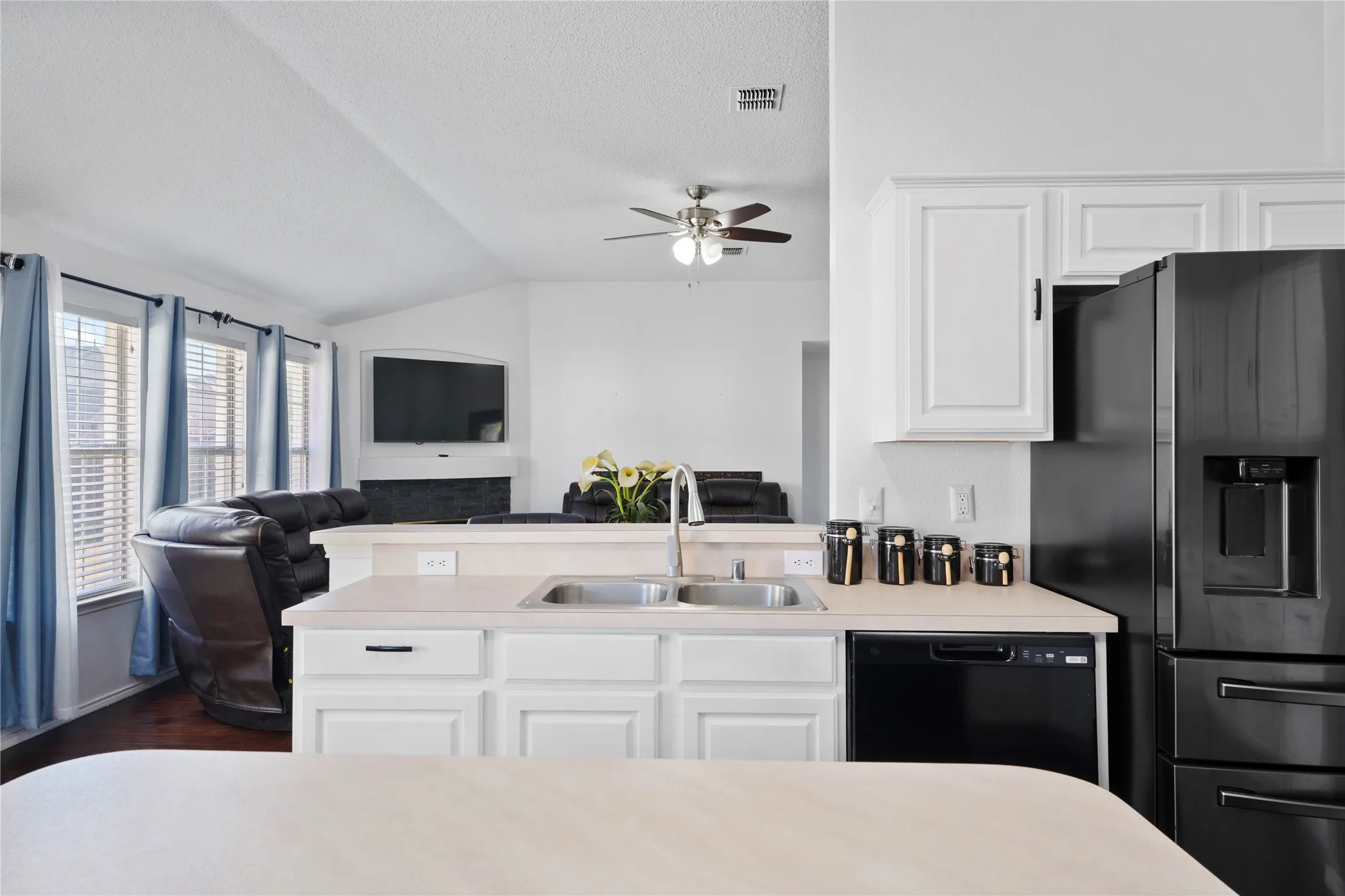 Kitchen with white cabinetry, stainless steel sink, black appliances, and light-toned countertops
