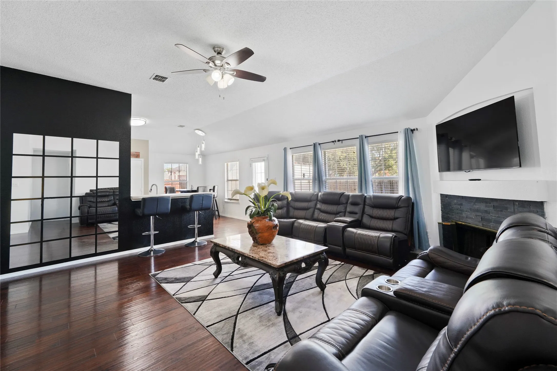Vaulted ceiling, wood-finish flooring, built-in fireplace with stone-tile surround, and multiple windows