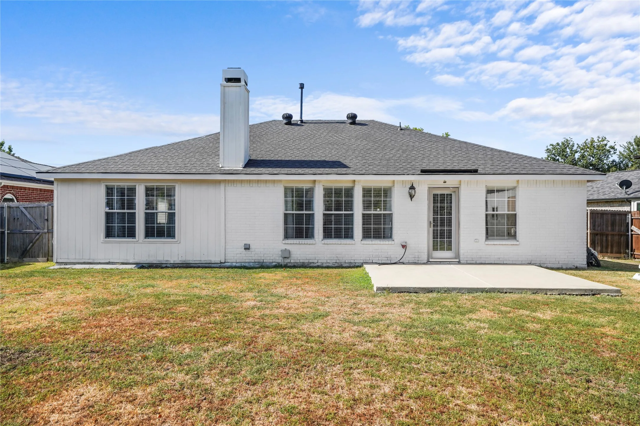 Rear exterior featuring multiple windows, a white brick facade, and a concrete patio