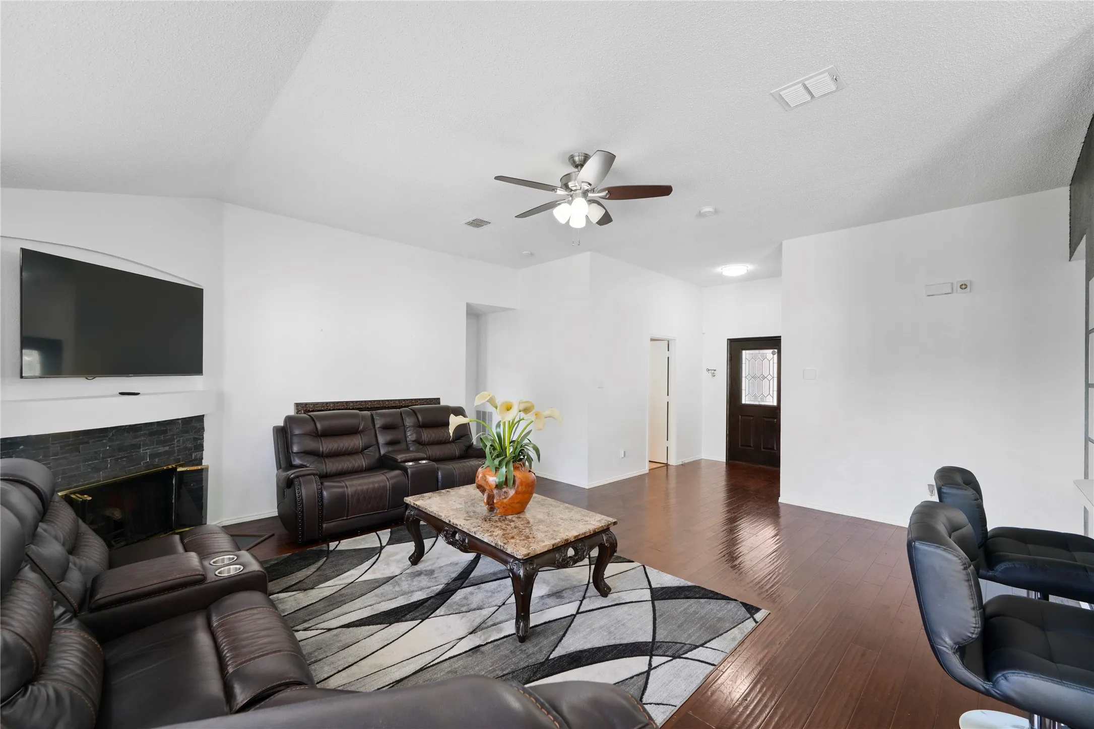 Vaulted ceiling living area featuring a dark brick fireplace, wood-finish flooring, and a ceiling fan