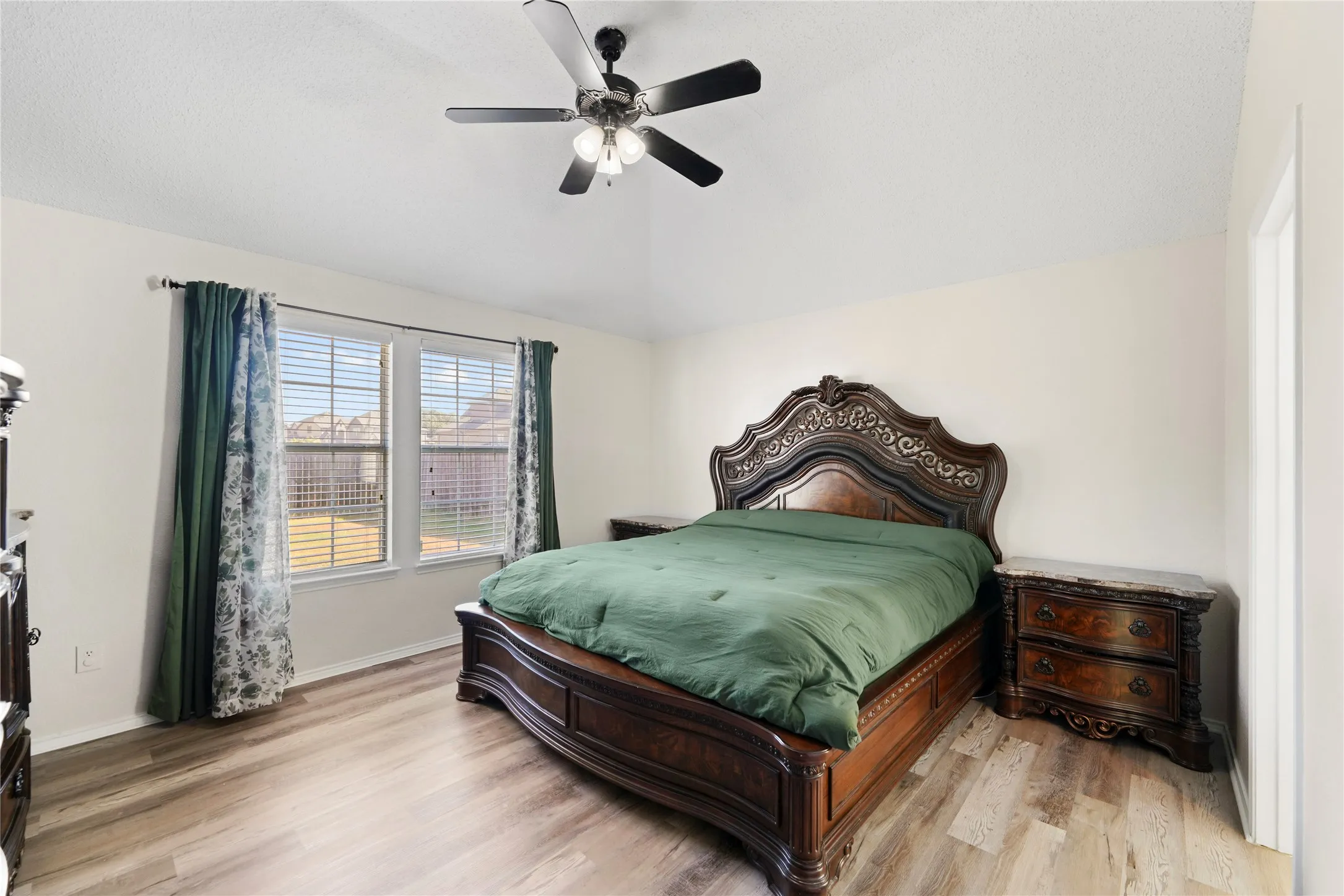 Vaulted ceiling, ceiling fan with light fixture, two windows, wood-finish flooring, and neutral wall tones