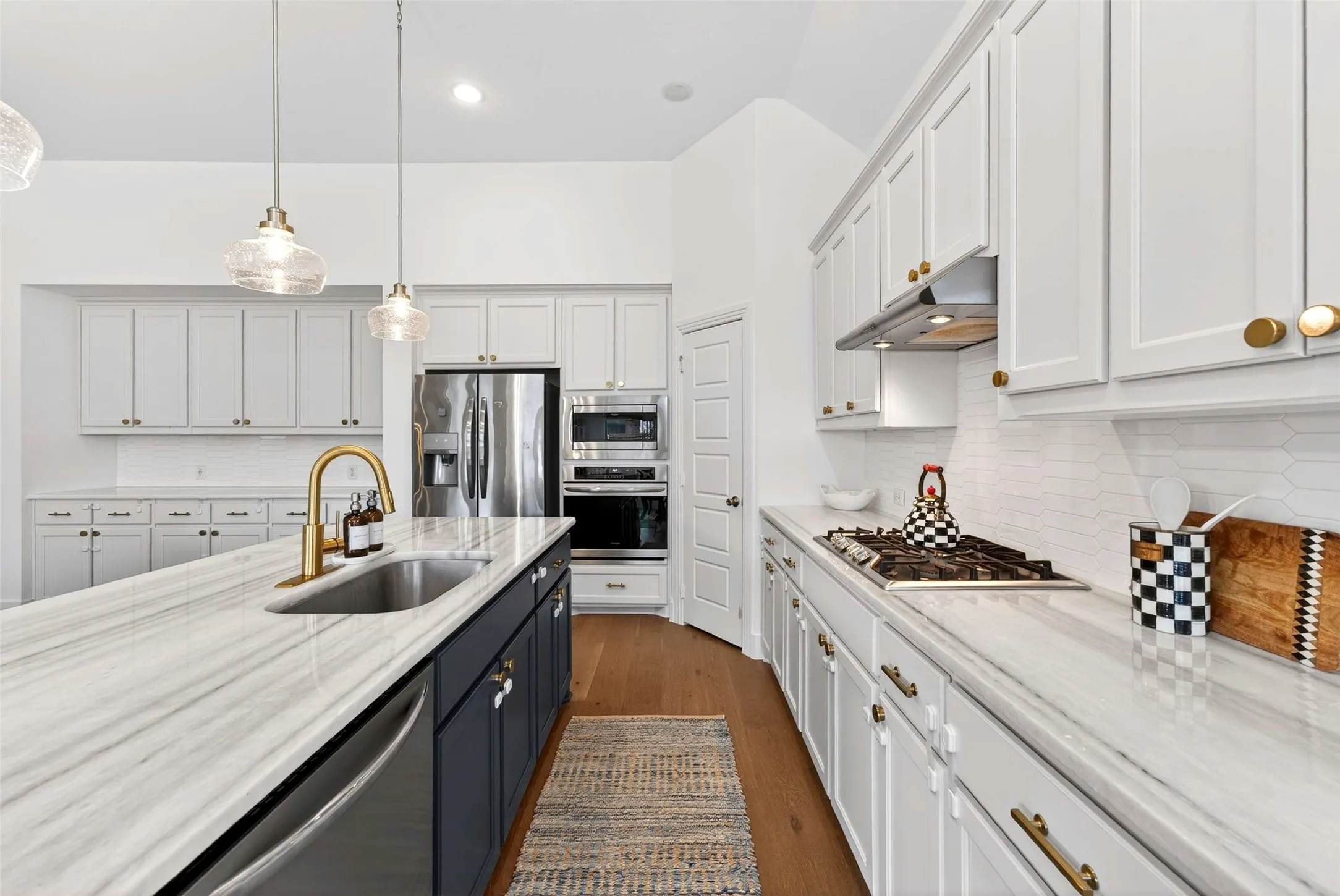 Kitchen featuring a dual-tone island with a stainless steel sink, gold-finish faucet, and pendant lighting