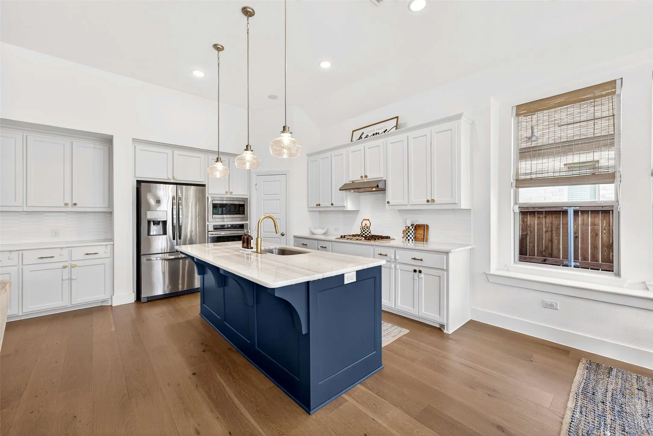 Vaulted ceiling kitchen featuring a blue island with a stone countertop, stainless steel appliances, wood-finish flooring, and white cabinetry
