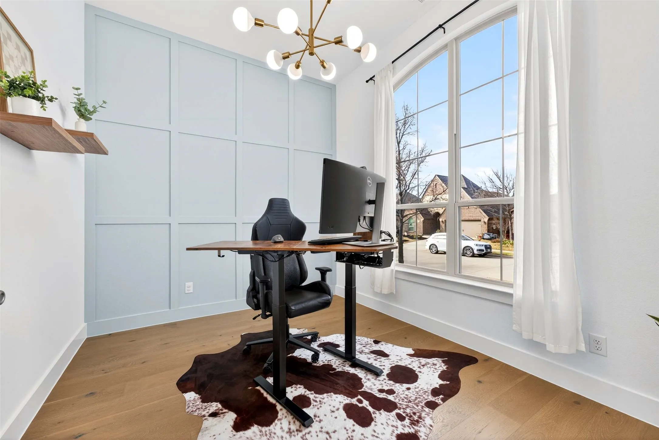 Hardwood flooring throughout, a large arched window with grid detailing, and a modern chandelier