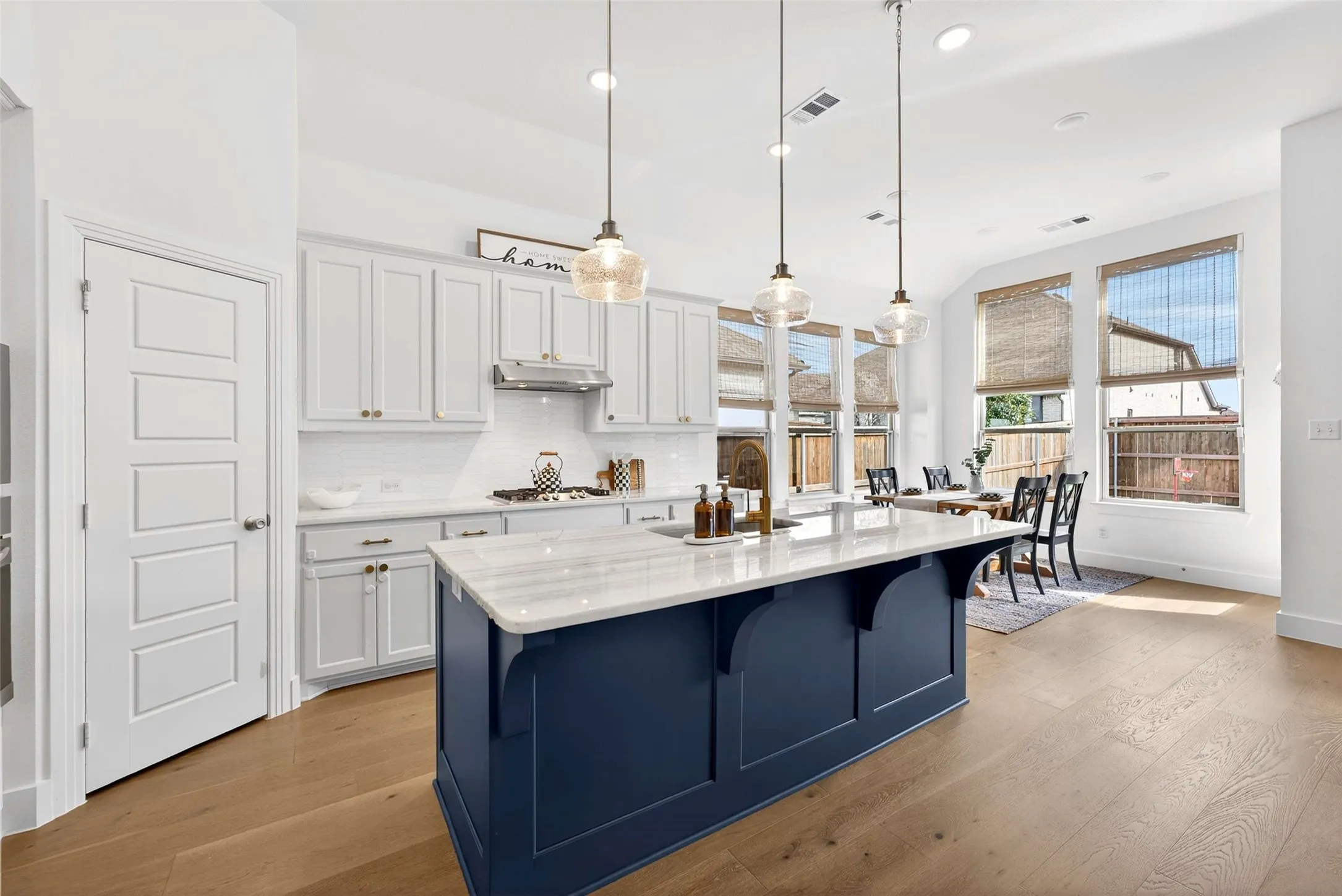Open-concept kitchen featuring a large island with a quartz countertop, pendant lighting, white shaker cabinetry, and wood-finish flooring