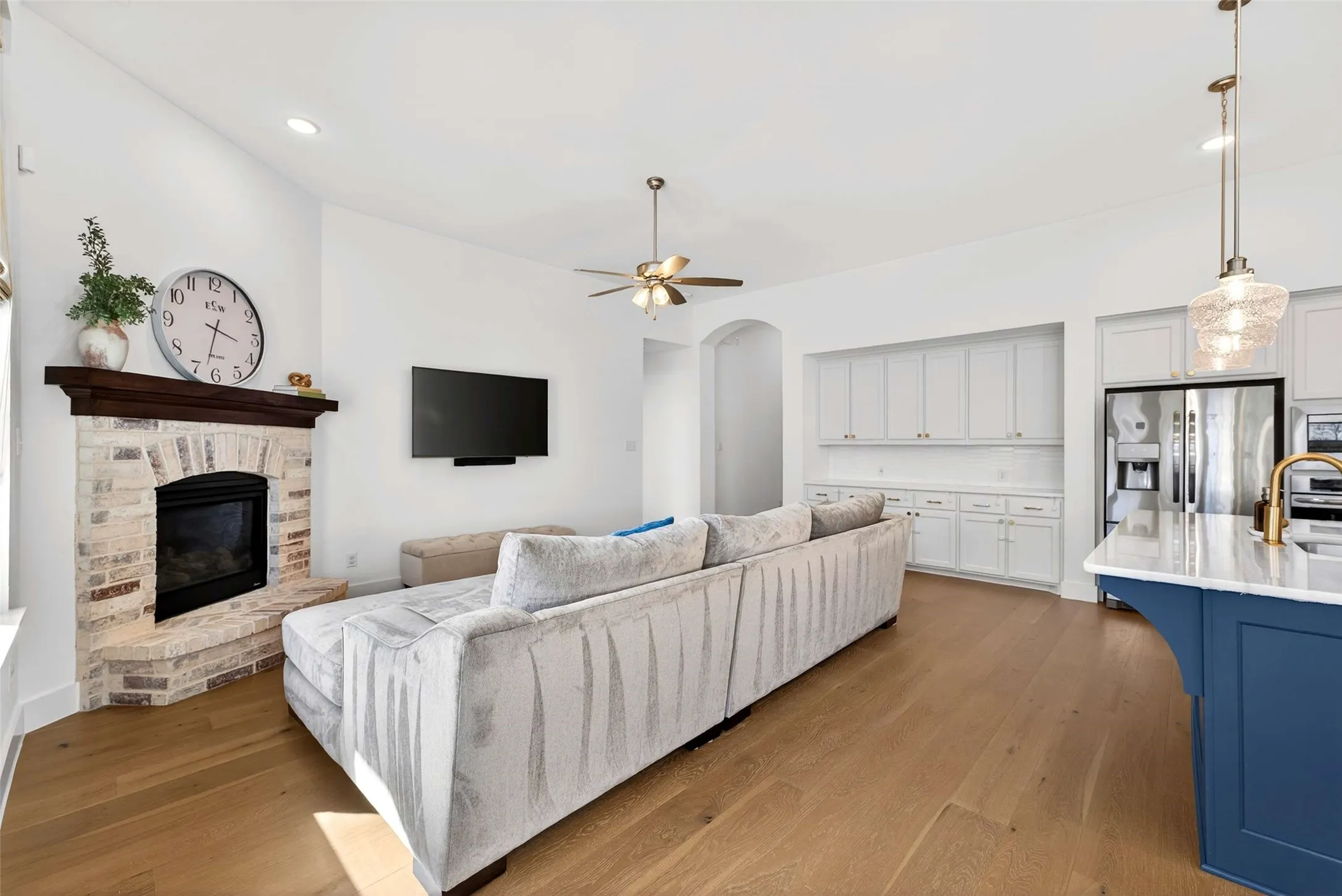 Hardwood flooring, brick fireplace with wood mantel, recessed lighting, ceiling fan, and built-in white cabinetry with marble-look countertop