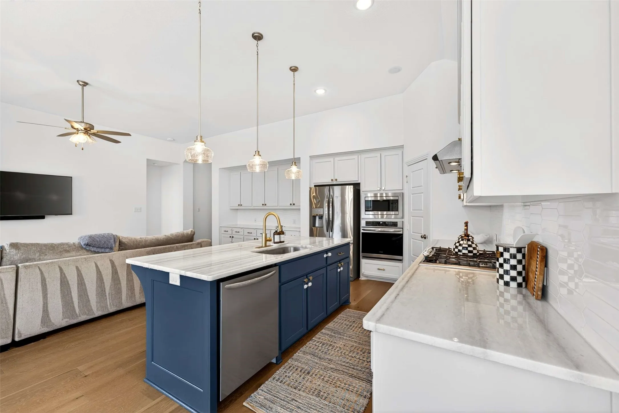 White cabinetry with stainless steel appliances, a center island with a sink and gold-finish faucet, white countertops, and wood-finish flooring