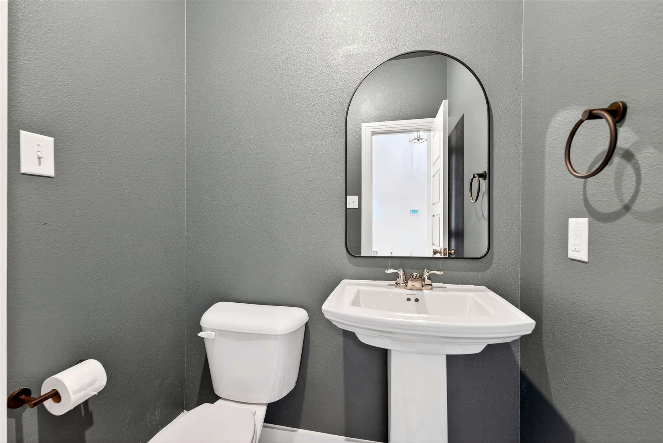 Pedestal sink with polished chrome faucet, arched mirror, and bronze-finish towel ring