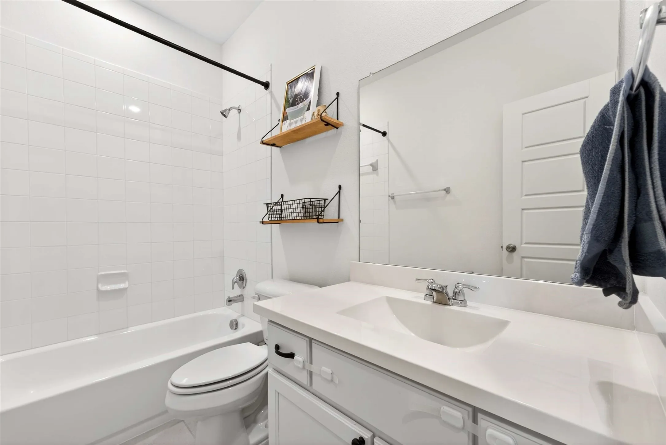 White subway tile tub surround, white vanity with integrated sink, chrome faucet, and large wall-mounted mirror