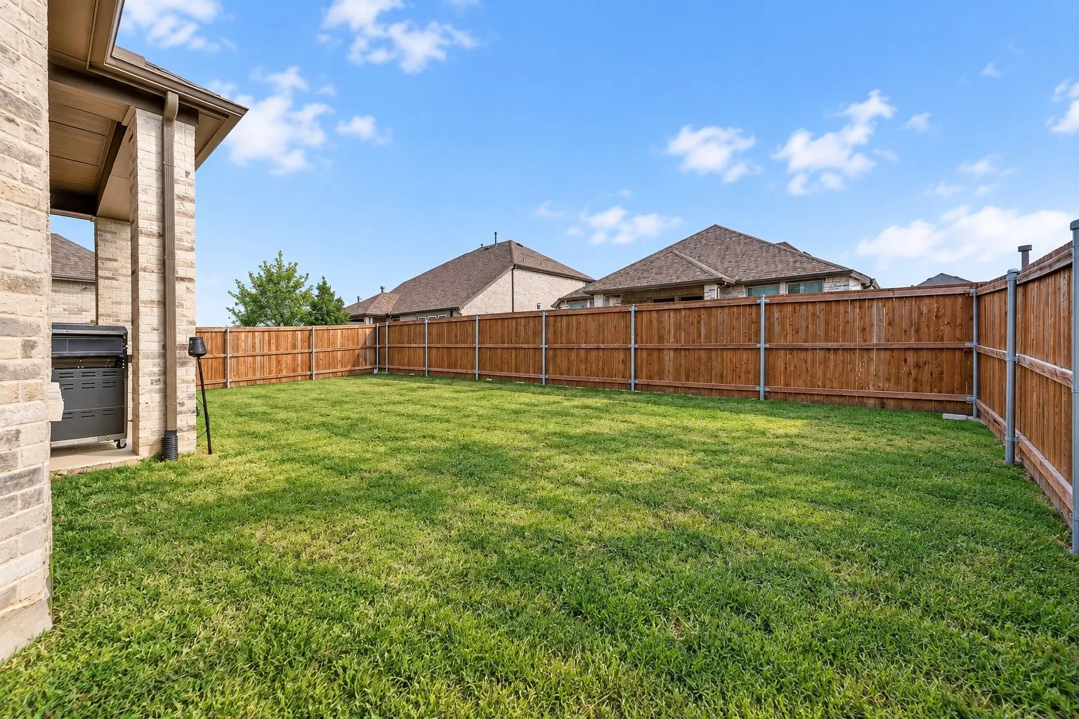 Spacious backyard featuring a wood privacy fence, green lawn, and brick exterior