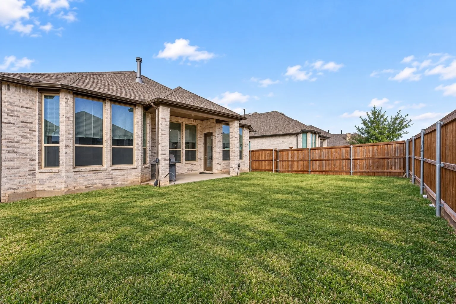 Expansive backyard with a manicured lawn, full privacy fencing, and a covered patio area