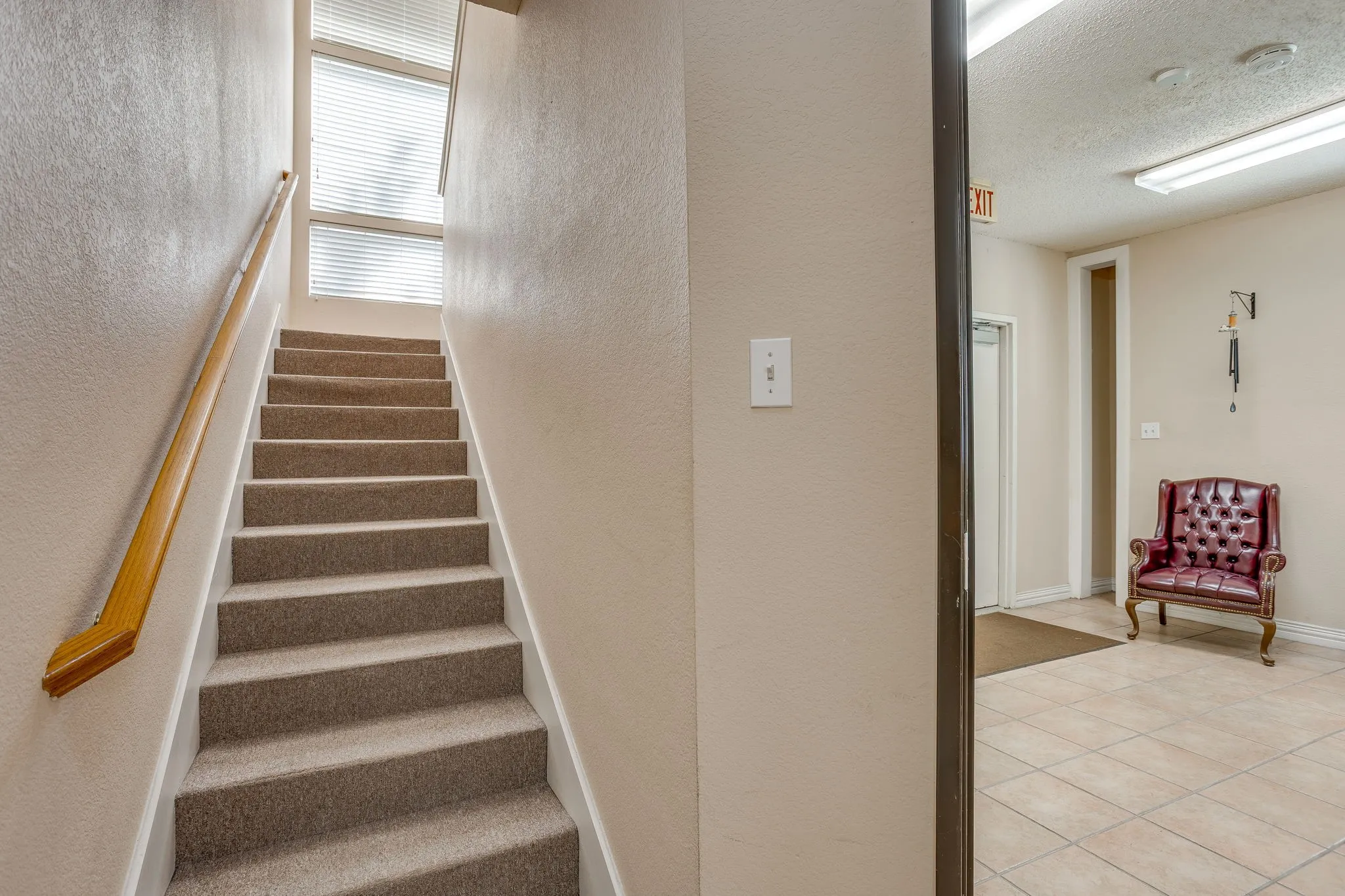 Carpeted staircase with wood handrail, upper-level window, and adjacent tiled flooring