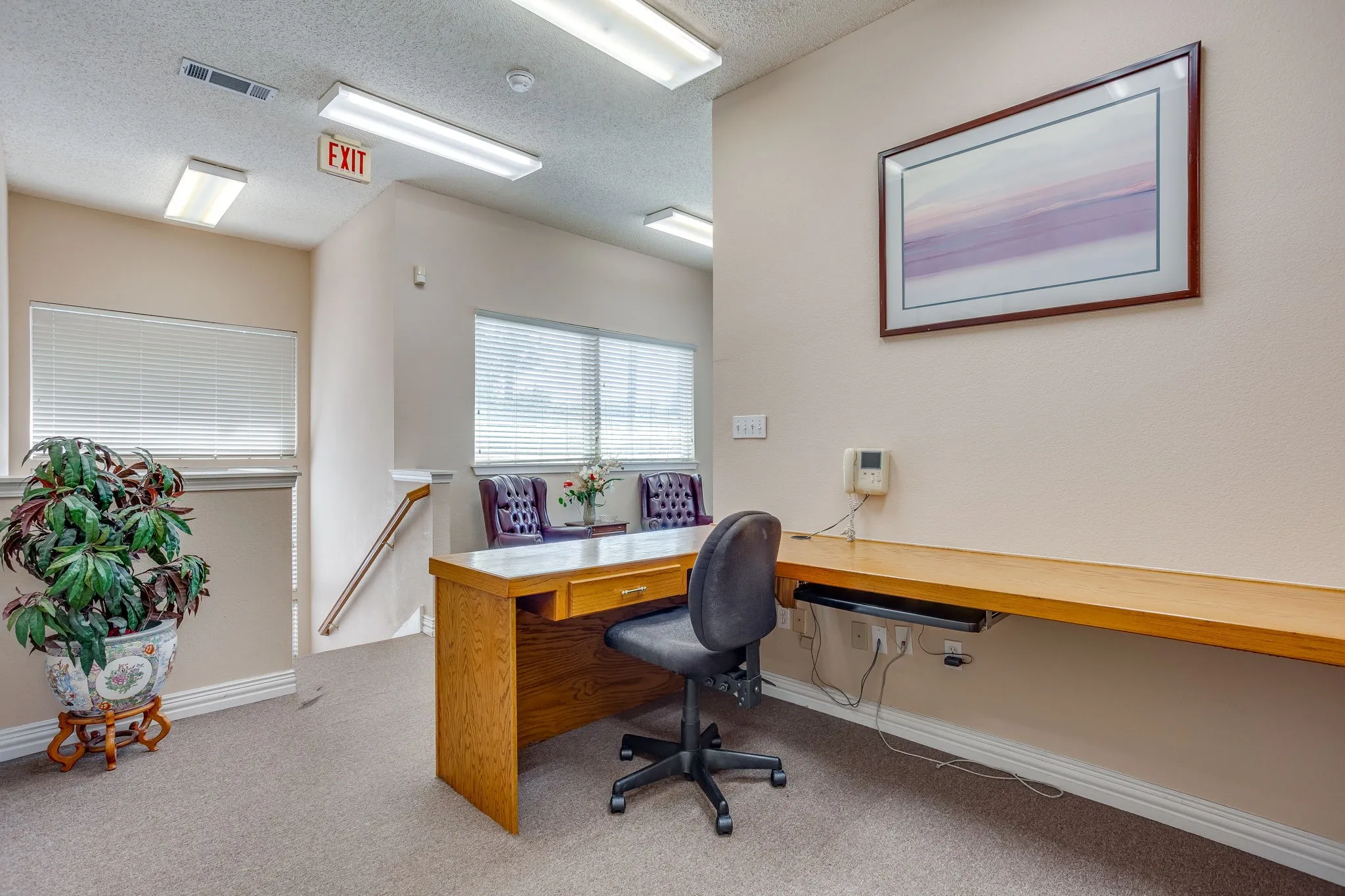 Carpeted office area featuring a built-in desk, wood-finish desktop, and multiple windows with blinds