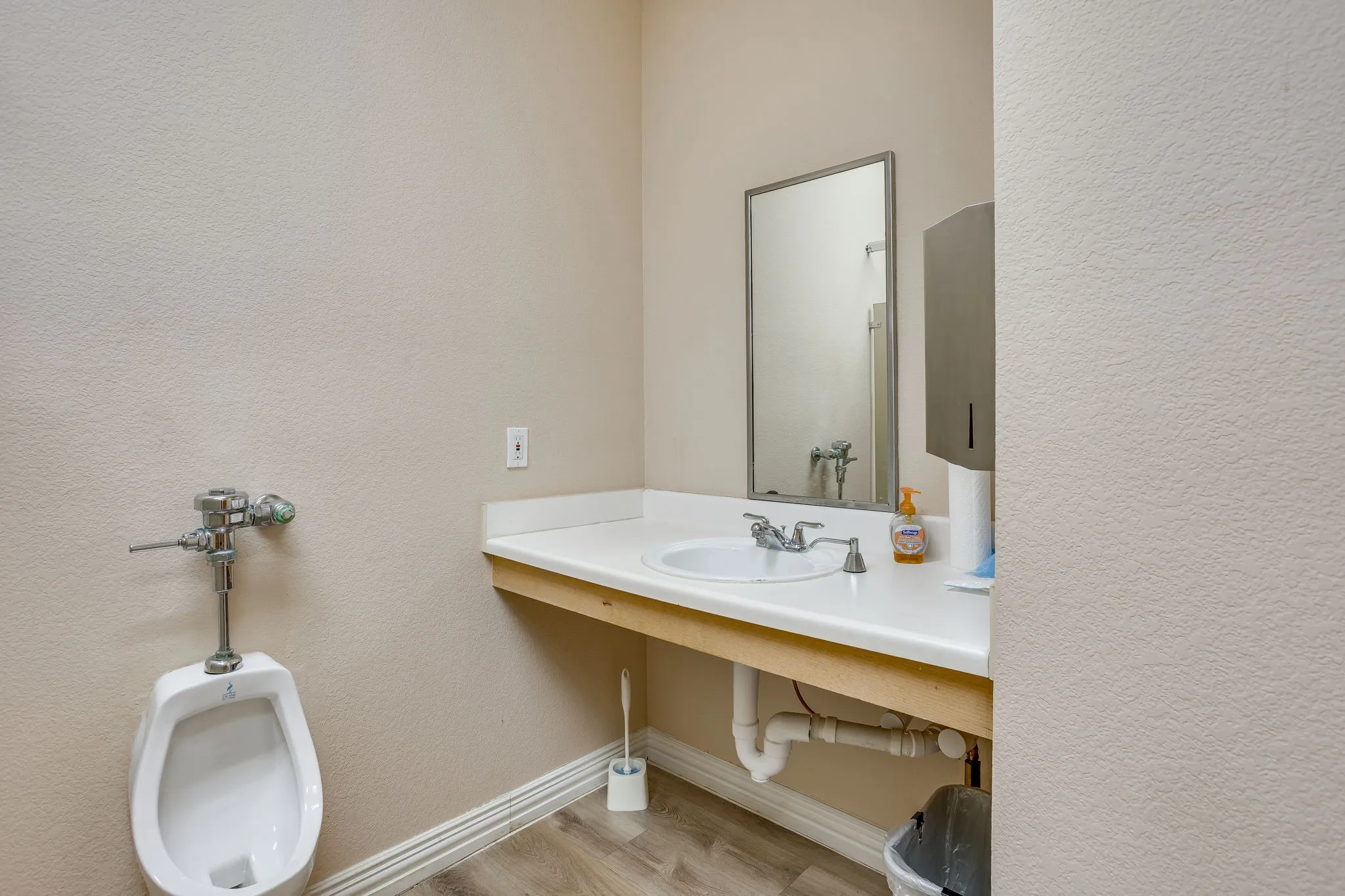 White wall-mounted urinal, single basin sink, laminate countertop, and wood-finish flooring
