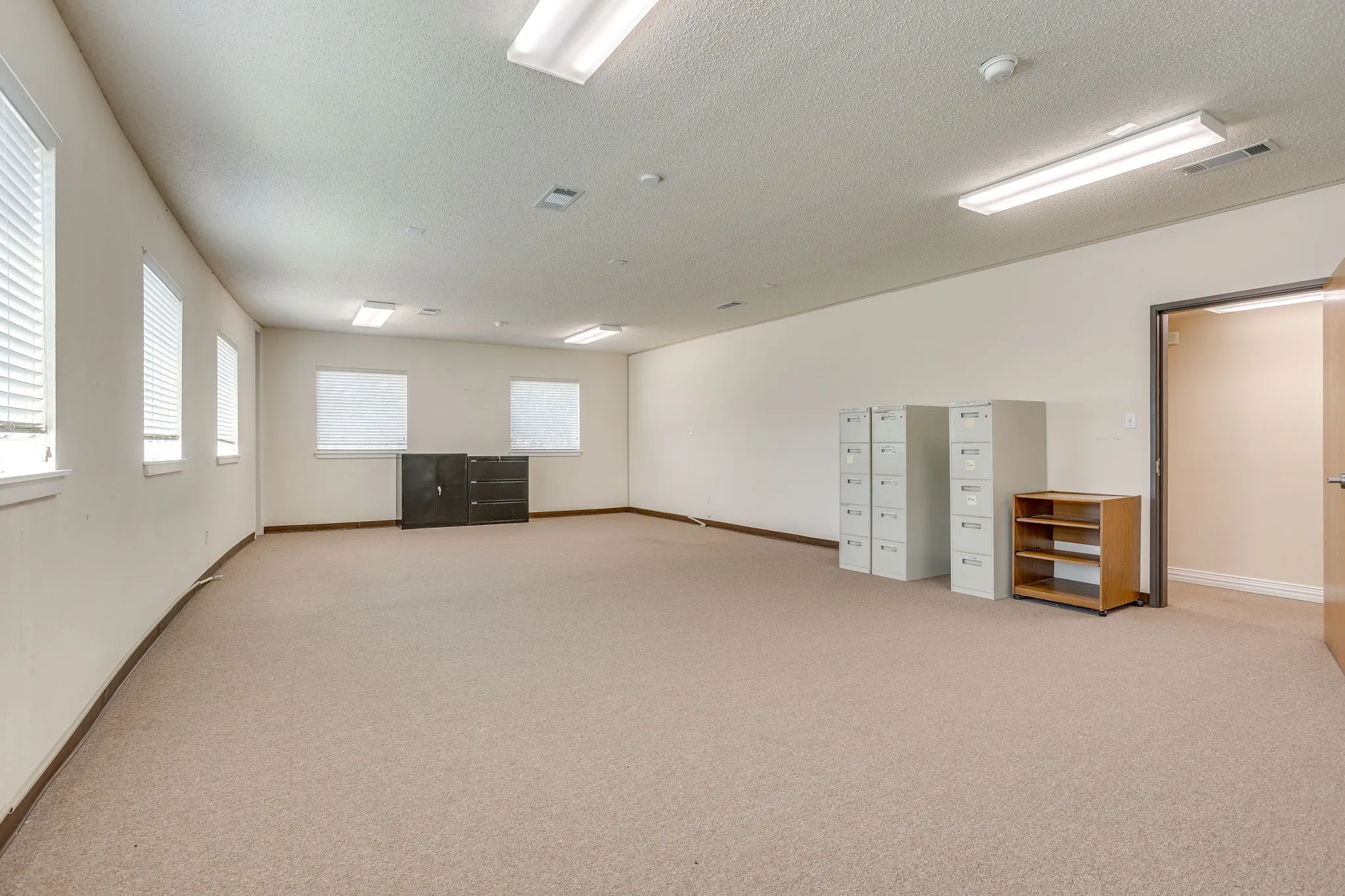 Spacious room with carpet flooring, multiple rectangular windows, recessed lighting, and a neutral color palette