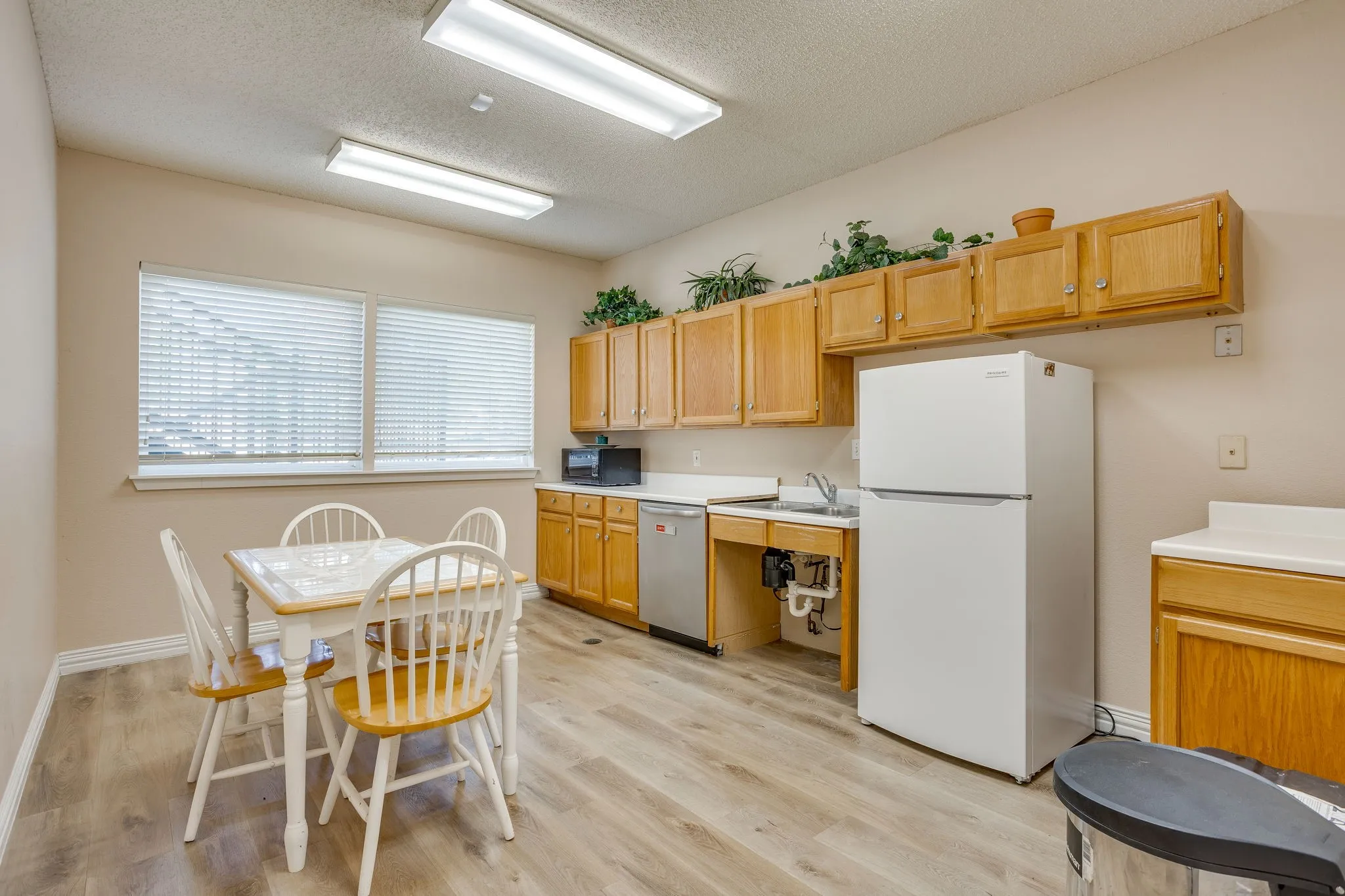 Kitchen area featuring wood-finish flooring, overhead fluorescent lighting, and two windows with blinds