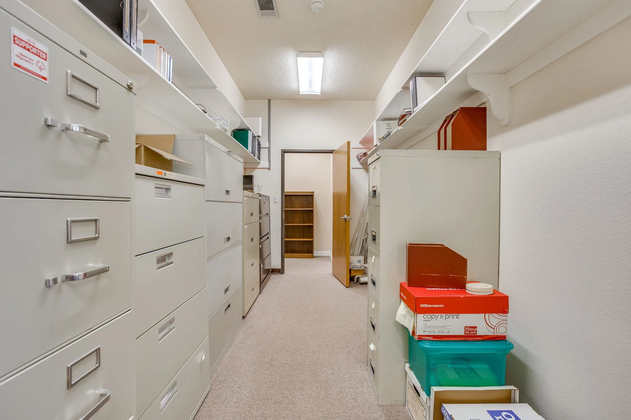 Recessed lighting illuminates the carpeted corridor, featuring built-in shelving and a doorway with a visible wooden frame