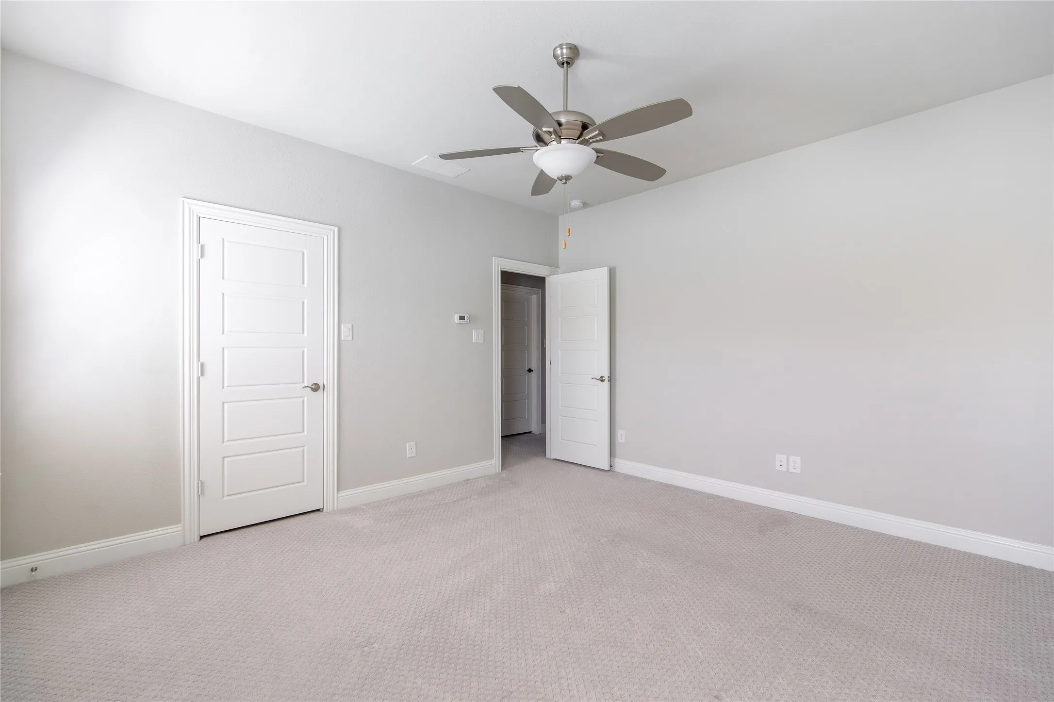 Light gray carpeted flooring, smooth light gray walls, white panel doors, and a ceiling fan with integrated lighting