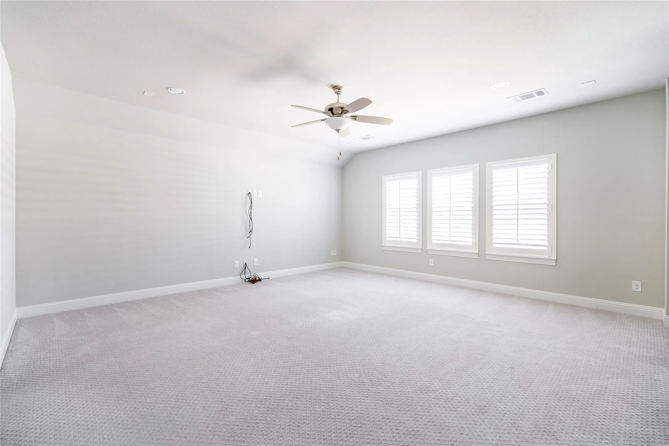 Recessed lighting, ceiling fan, three windows with plantation shutters, light gray wall paint, and gray carpeting