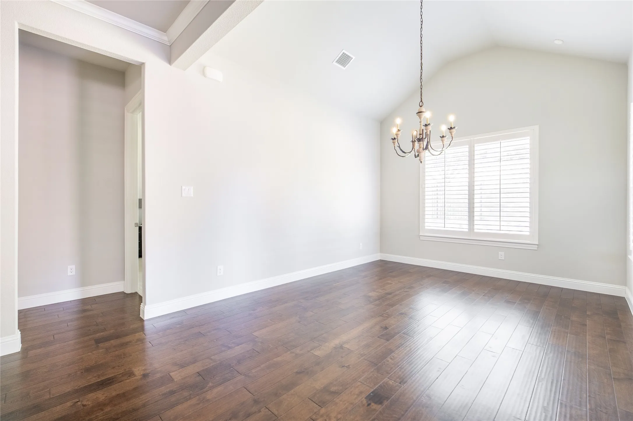 Vaulted ceiling with a chandelier, wood-finish flooring, and window with plantation shutters