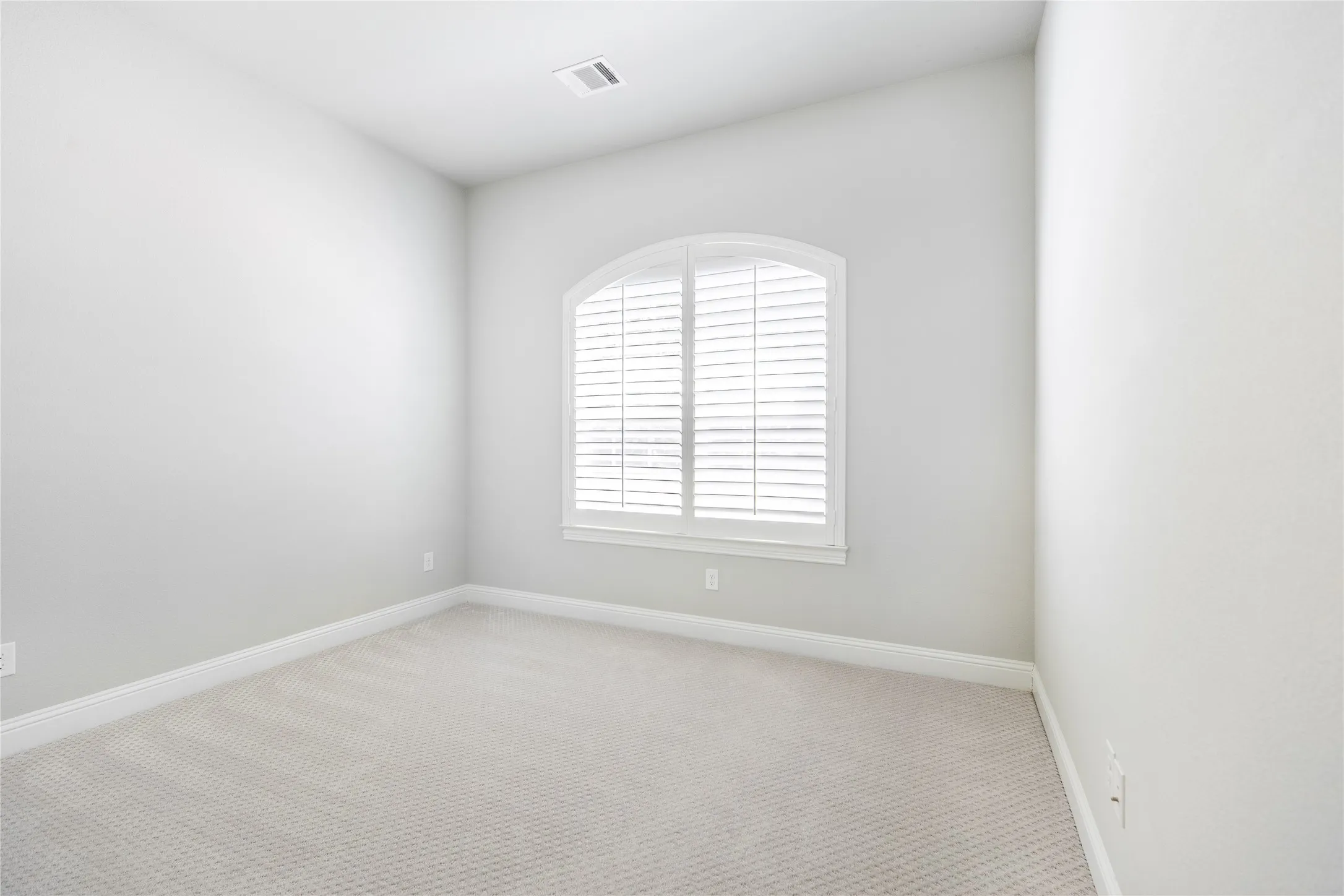 Arched window with plantation shutters, light-toned carpeting, and a neutral wall finish
