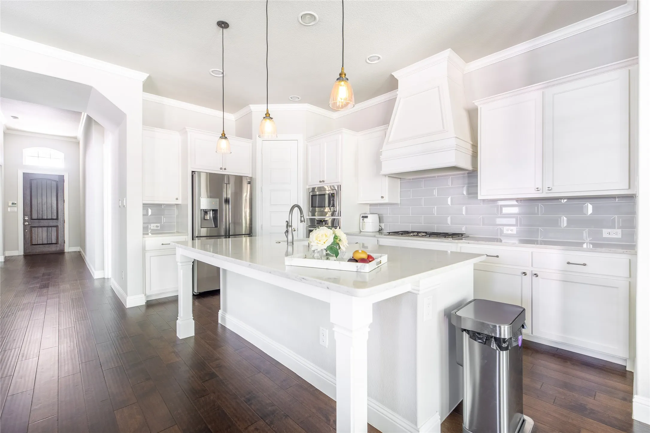 Kitchen featuring a large island, wood-finish flooring, white cabinetry, integrated stainless steel appliances, and a tile backsplash