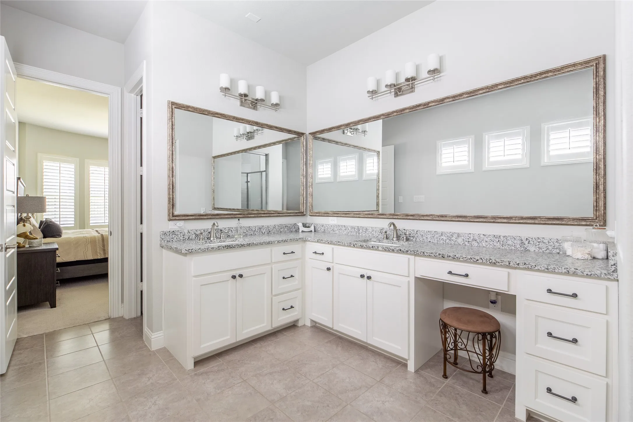 Dual vanity with white cabinetry, stone countertops, and large framed mirrors