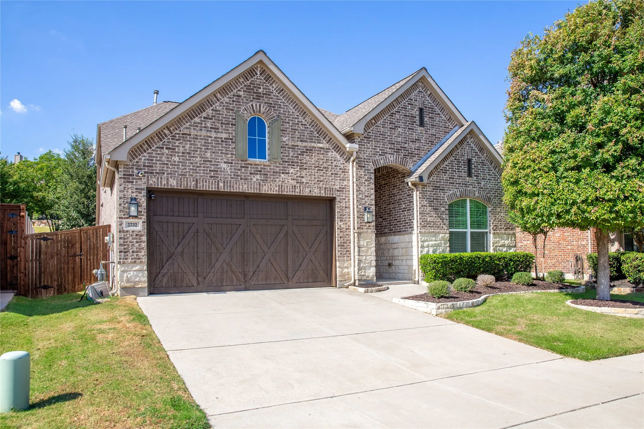 Brick and stone exterior with arched window details, an integrated garage with a wood-finish door, and structured landscaping