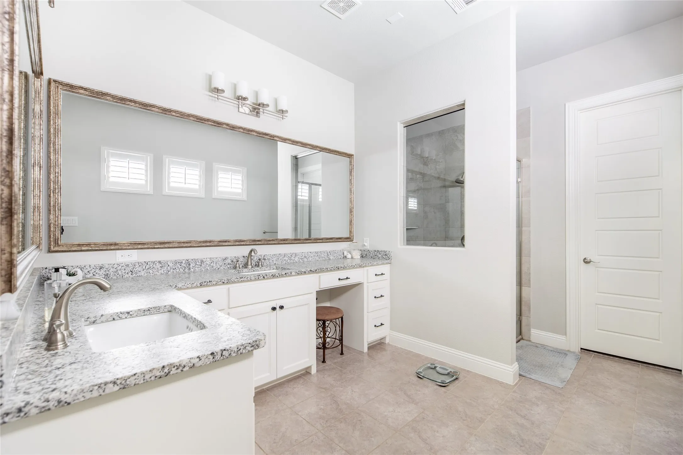 Dual vanity with undermount sinks, speckled stone countertops, and white cabinetry