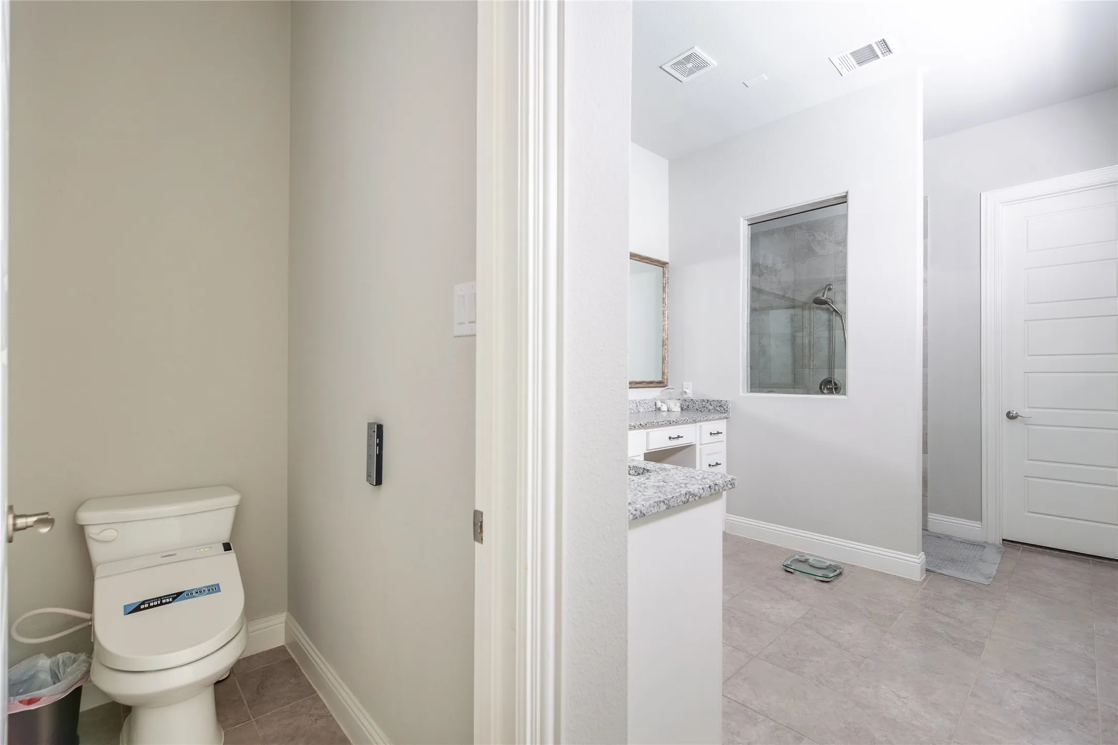 Tile flooring, white paneled door, built-in vanity with granite countertop, recessed lighting, and a walk-in shower with a framed window