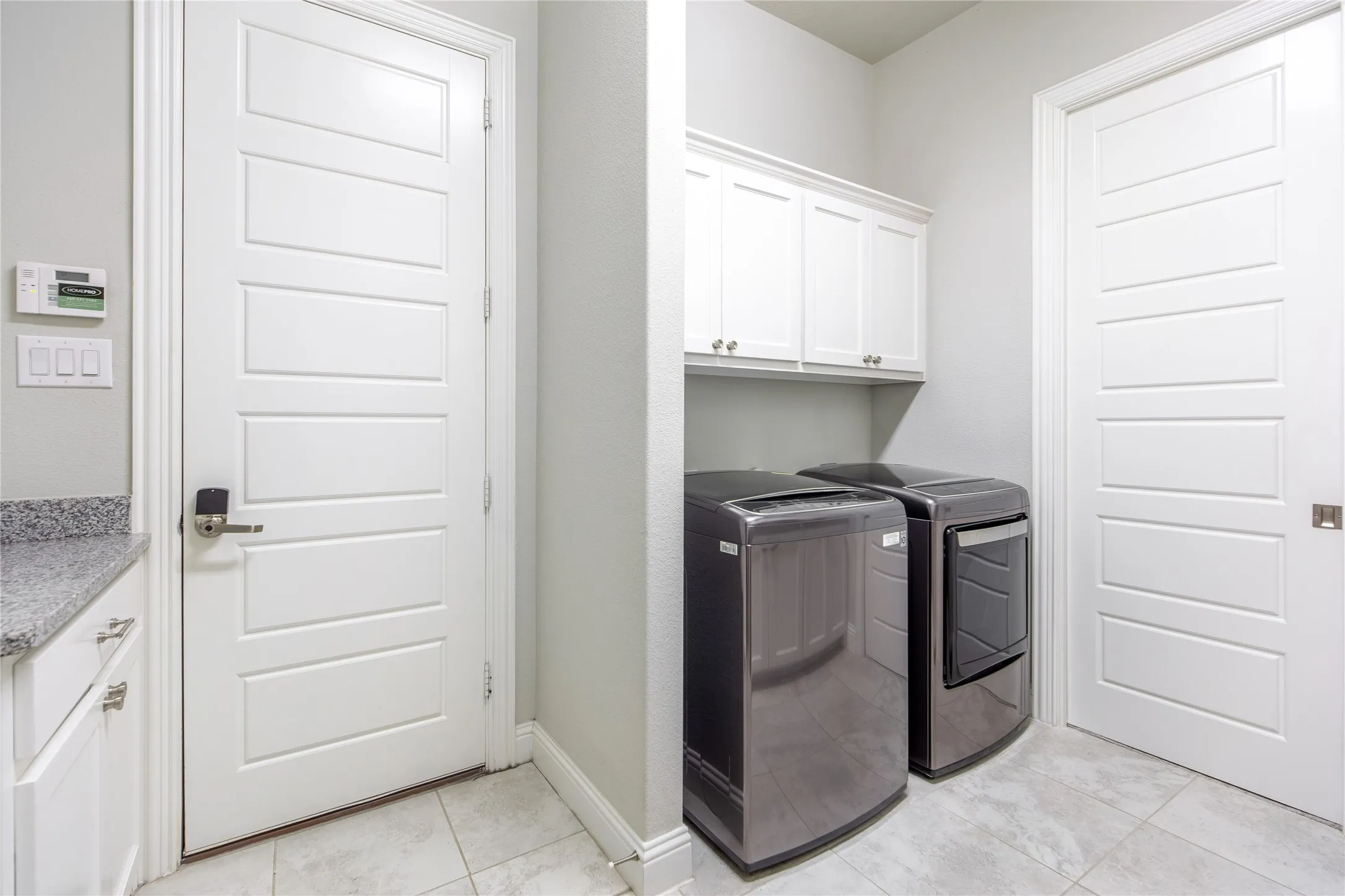 Laundry area featuring white cabinetry, a light gray countertop, and light-toned tile flooring