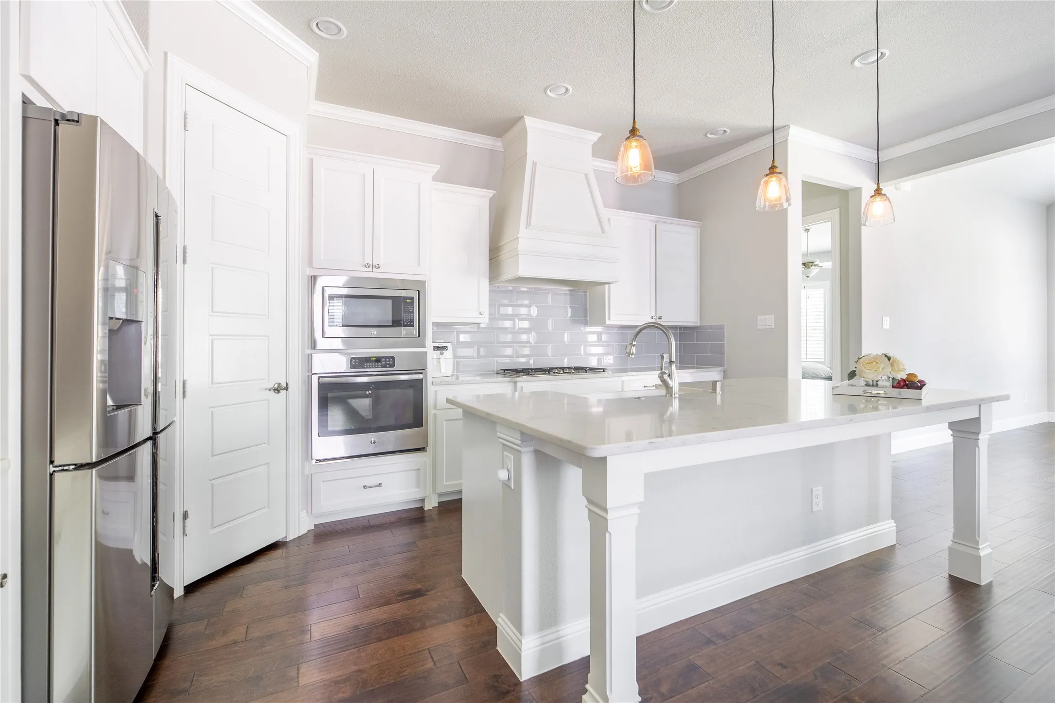Kitchen featuring a central island with a light-toned countertop, stainless steel appliances, wood-finish flooring, white cabinetry, and pendant lighting
