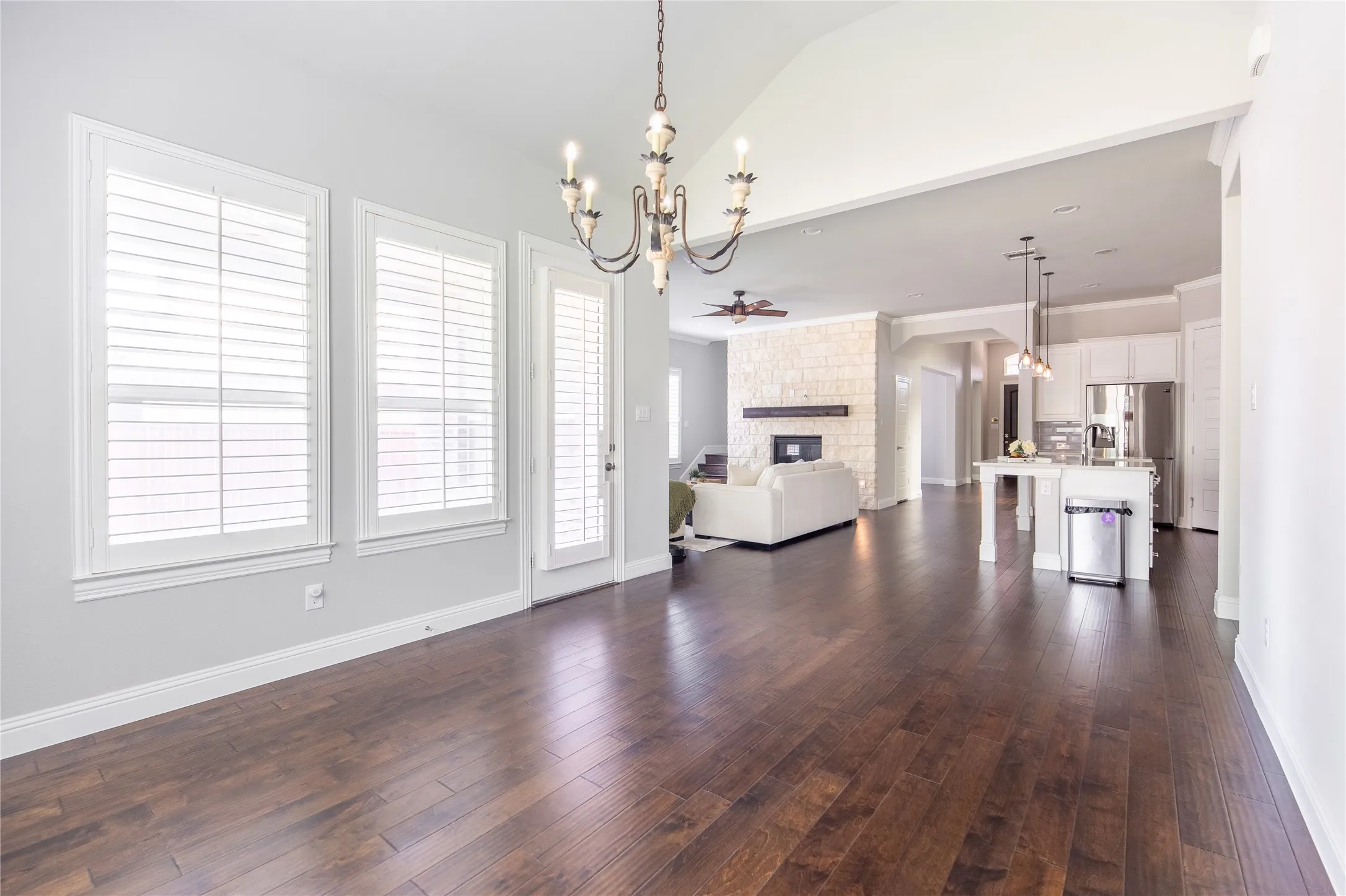 Vaulted ceiling with an ornate chandelier, wood-finish flooring, plantation shutters, and a stone fireplace