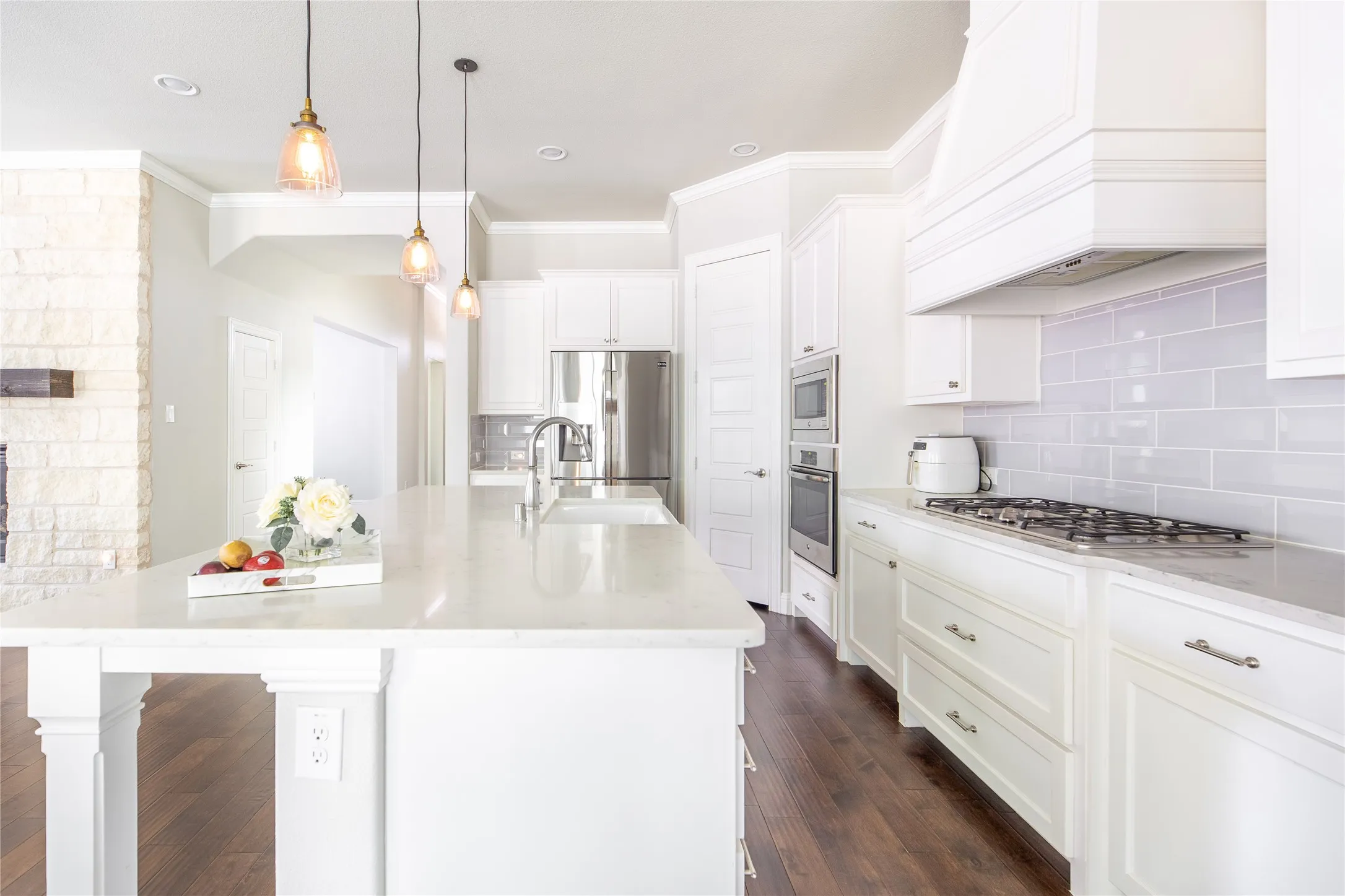 Gourmet kitchen featuring white cabinetry, stainless steel appliances, a gas range, a large center island with a sink, and pendant lighting
