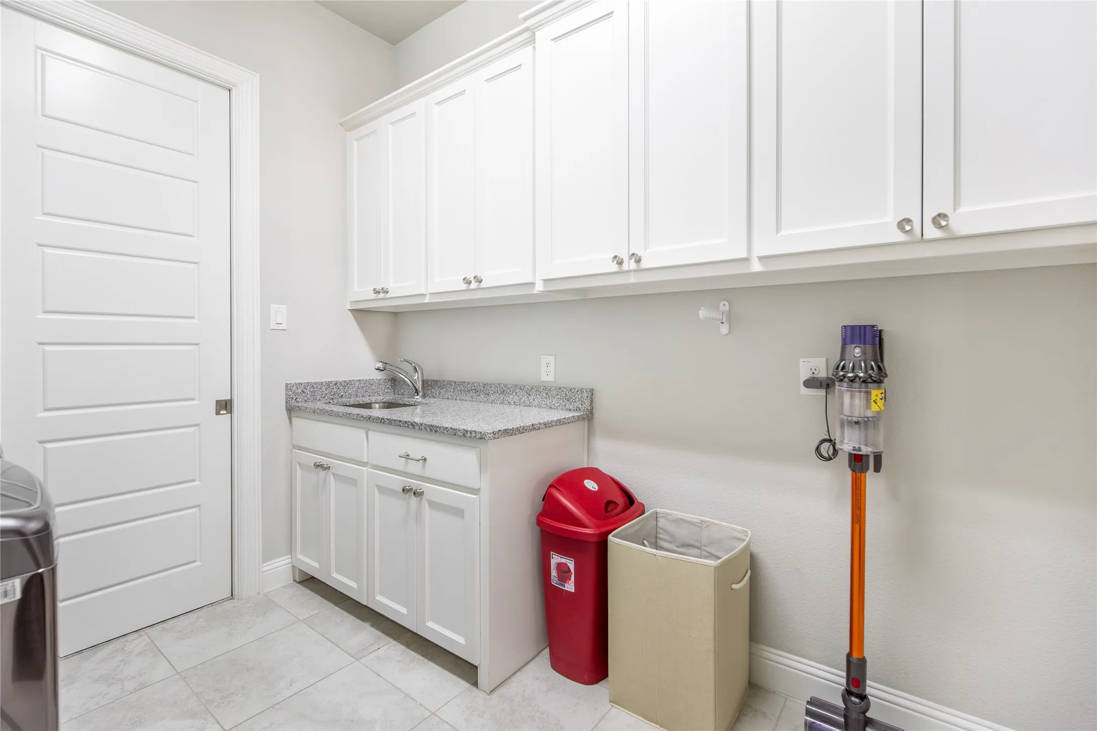 White cabinetry, granite-finish countertop, stainless steel sink, and tile flooring