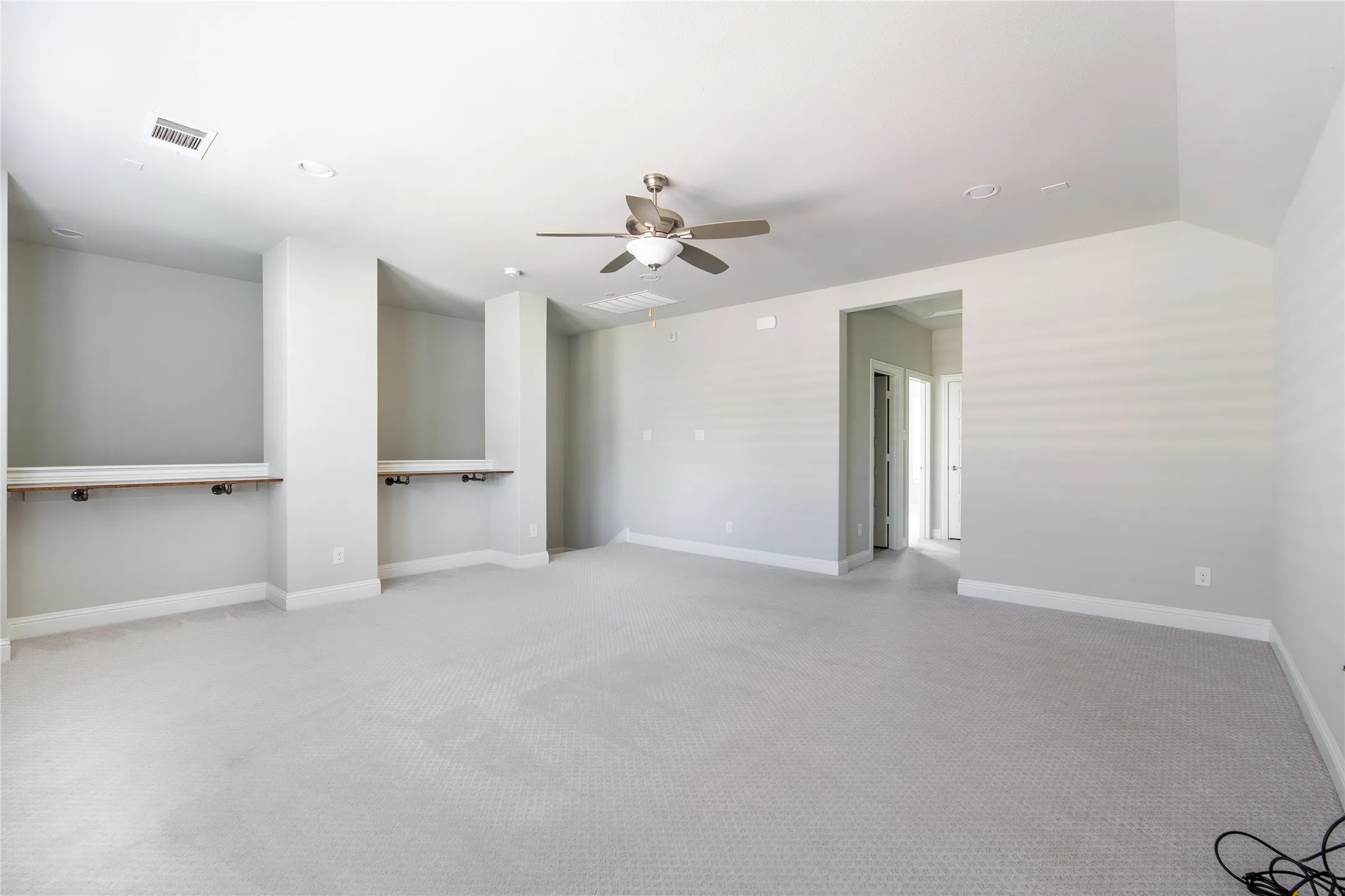 Spacious room featuring neutral carpeting, recessed lighting, ceiling fan, and two built-in desk nooks with wood-finish tops