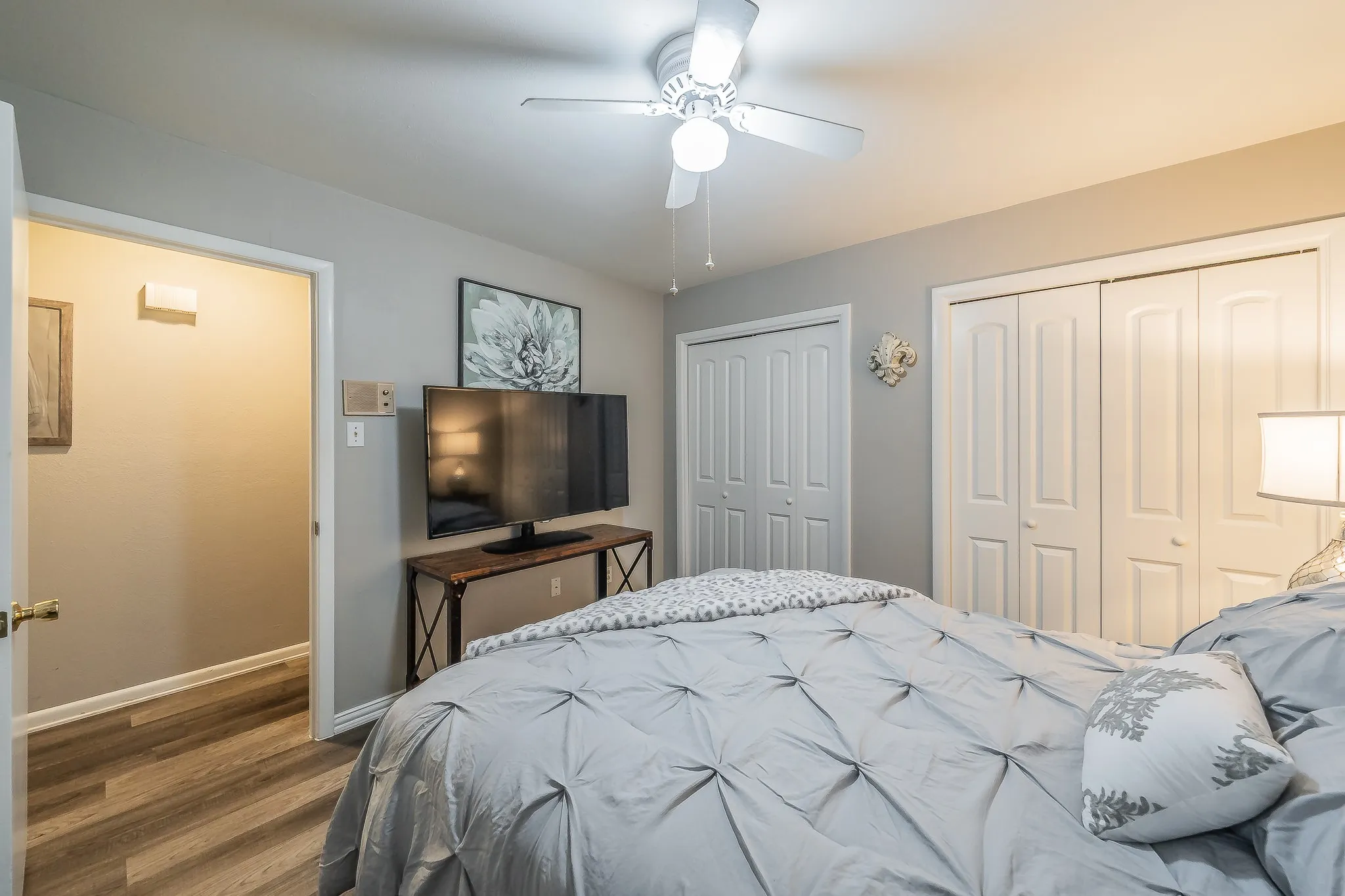 Wood-finish flooring throughout, ceiling fan with integrated lighting, dual bifold closet doors, and light gray wall paint