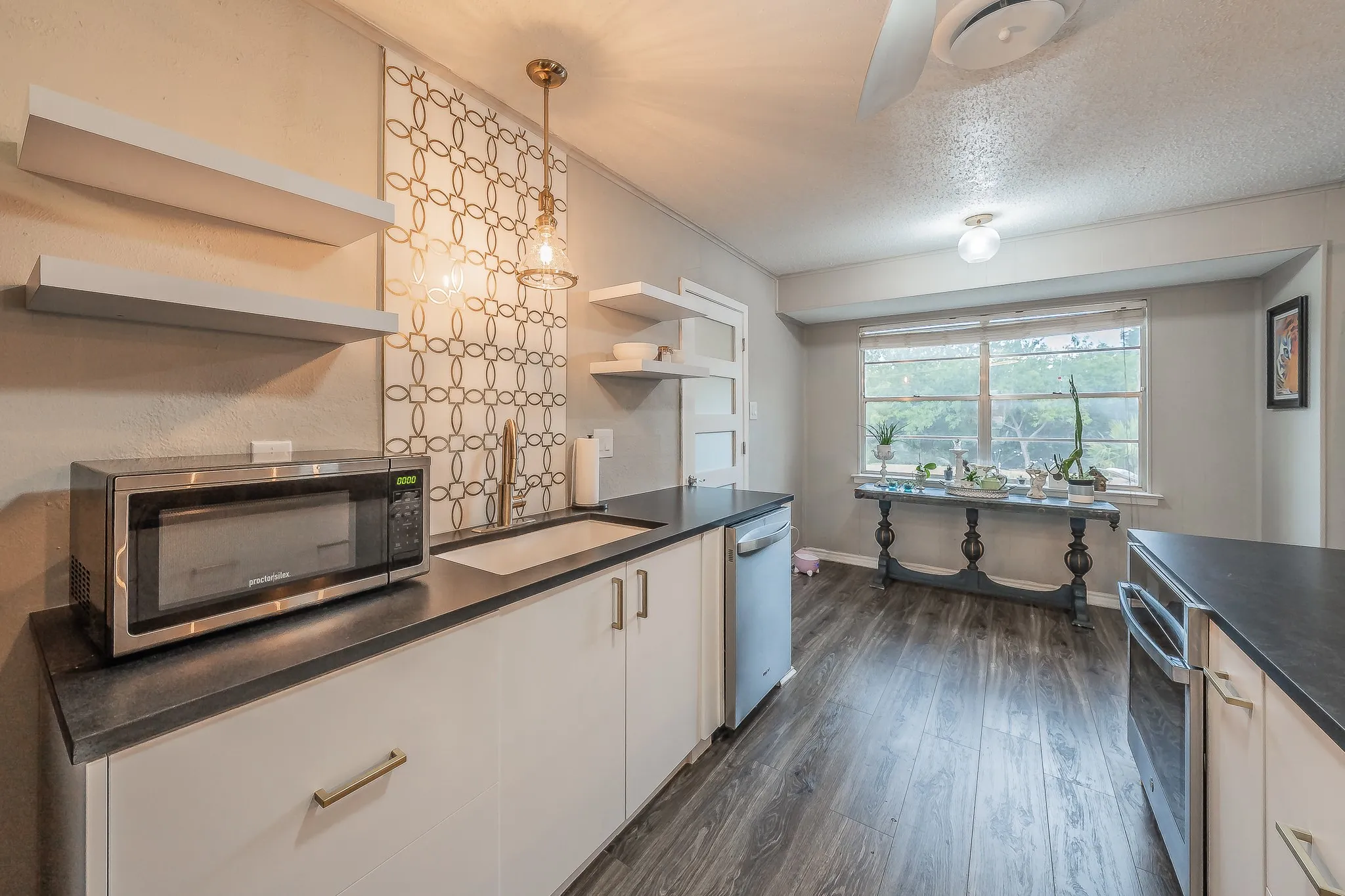 Kitchen featuring dark wood-finish flooring, white cabinetry with gold-tone hardware, dark countertops, and a full-size window