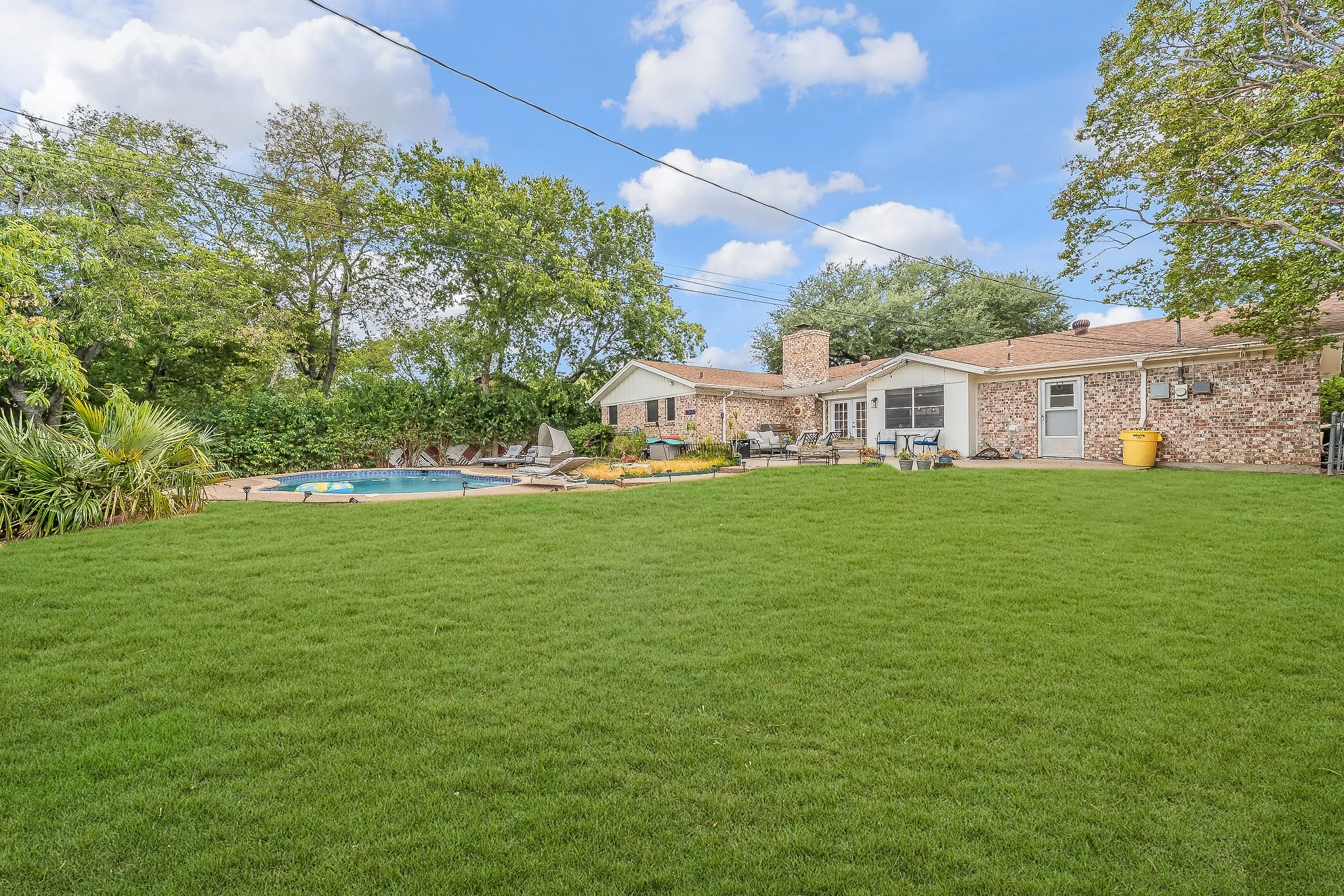 Spacious backyard featuring a rectangular swimming pool, mature trees, and a stone-clad exterior