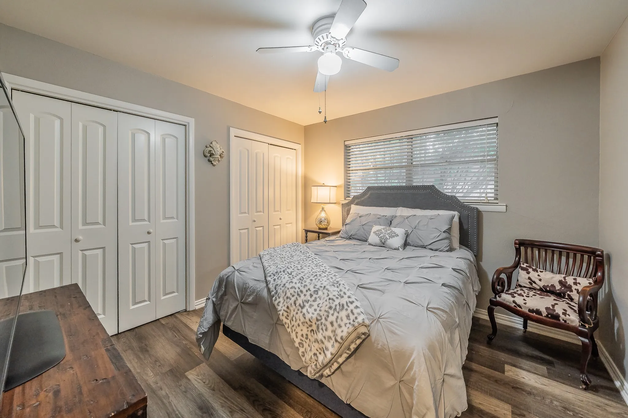 Wood-finish flooring, white bi-fold closet doors, ceiling fan with integrated lighting, window with blinds, and neutral wall paint