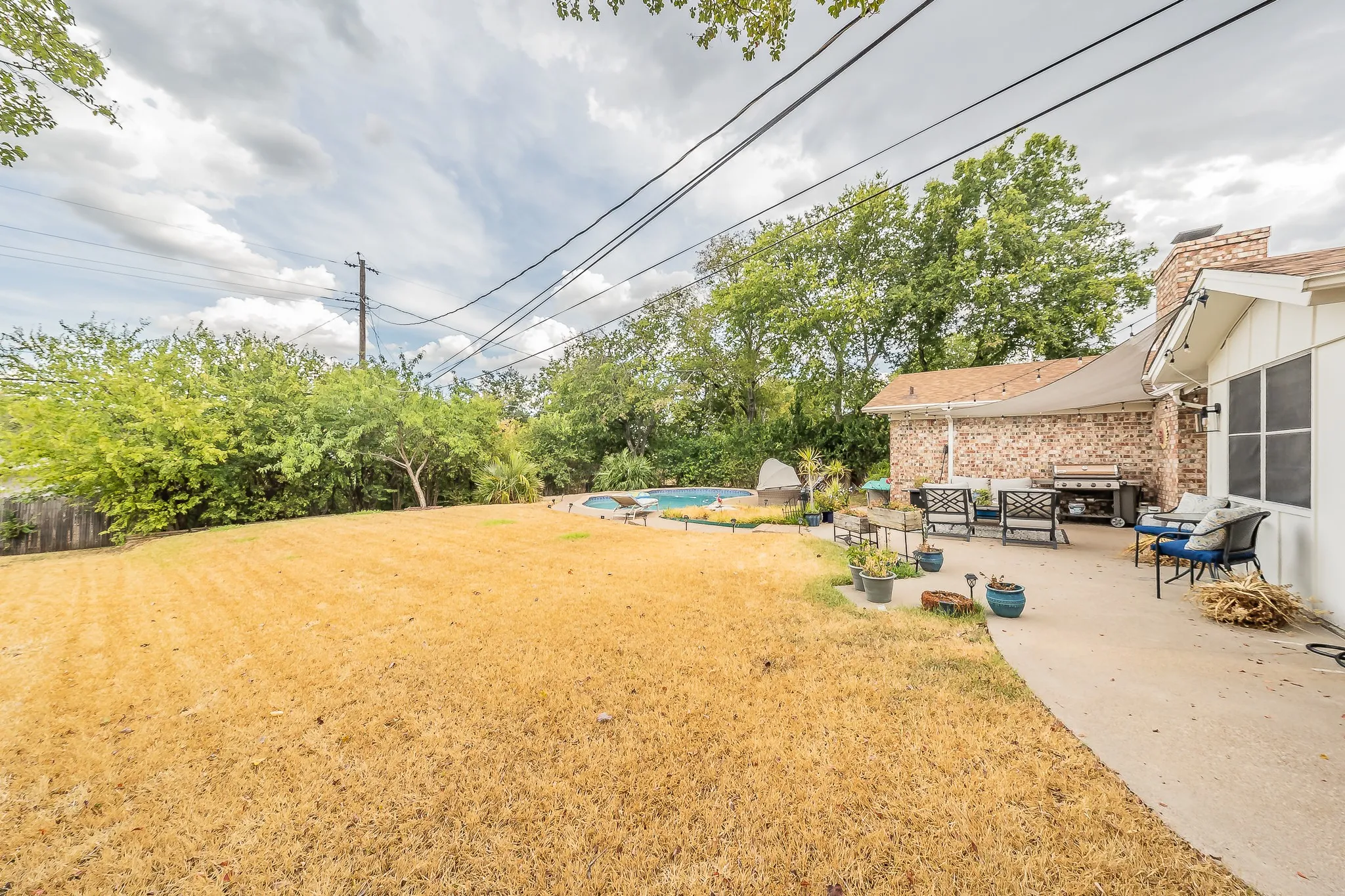 Expansive backyard featuring a concrete patio, brick exterior, and an in-ground swimming pool