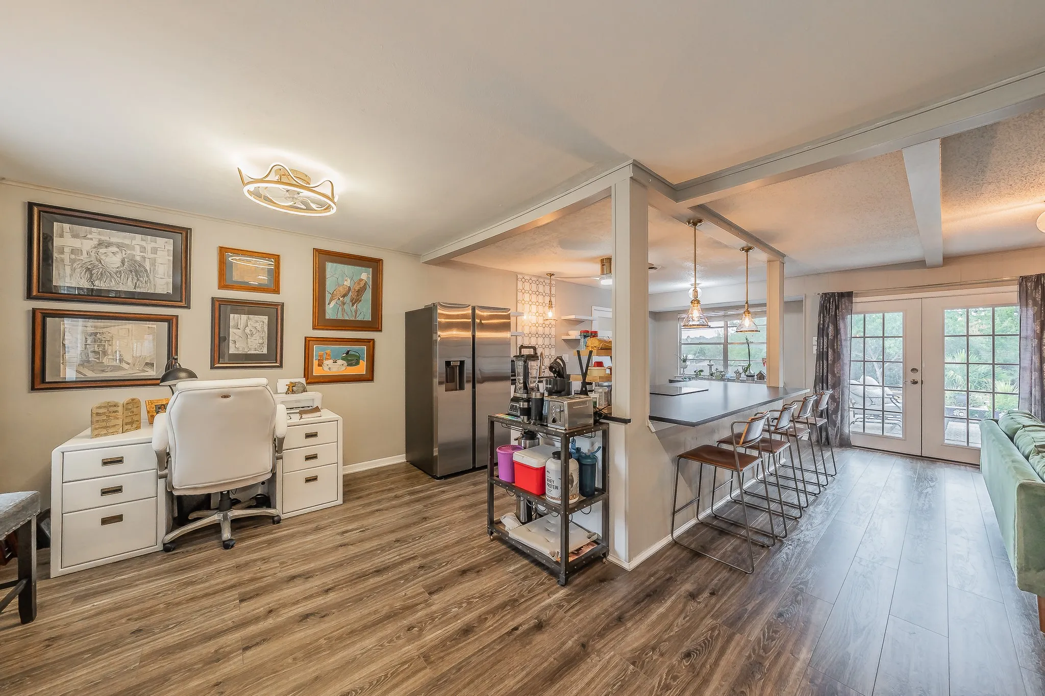 Open-concept living space with wood-finish flooring, a built-in breakfast bar, and multiple pendant light fixtures