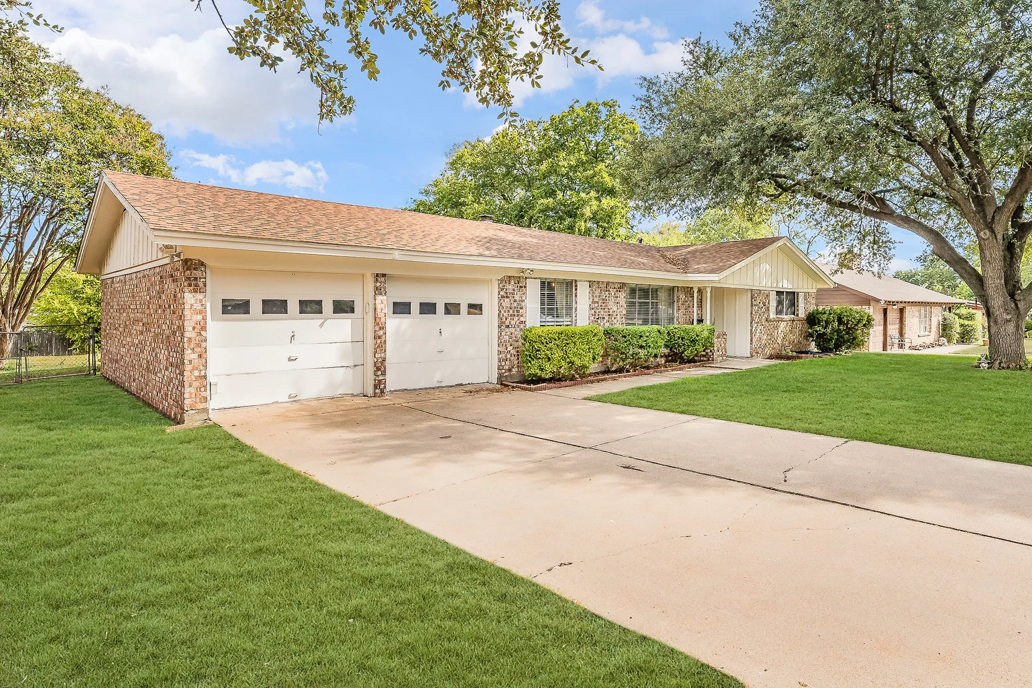 Brick exterior residence with a two-car garage, concrete driveway, and mature landscaping