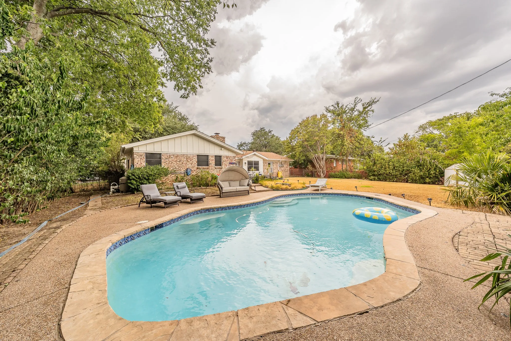 Freeform swimming pool with stone coping and a surrounding aggregate patio